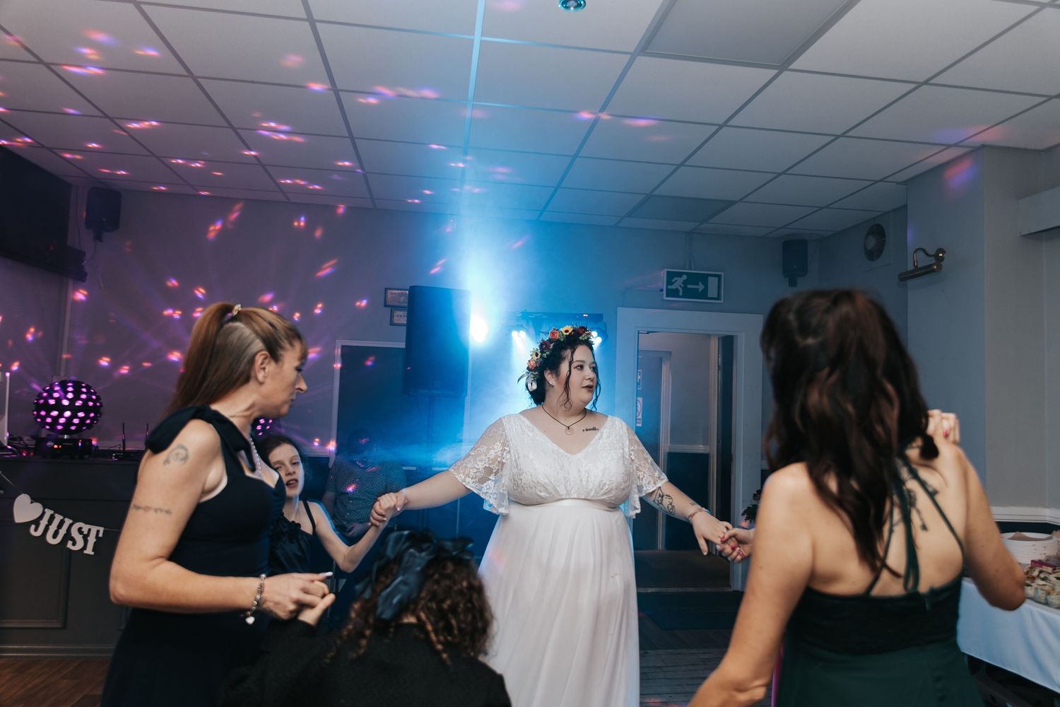 People dancing together at a wedding reception with colorful disco lights illuminating the dance floor.