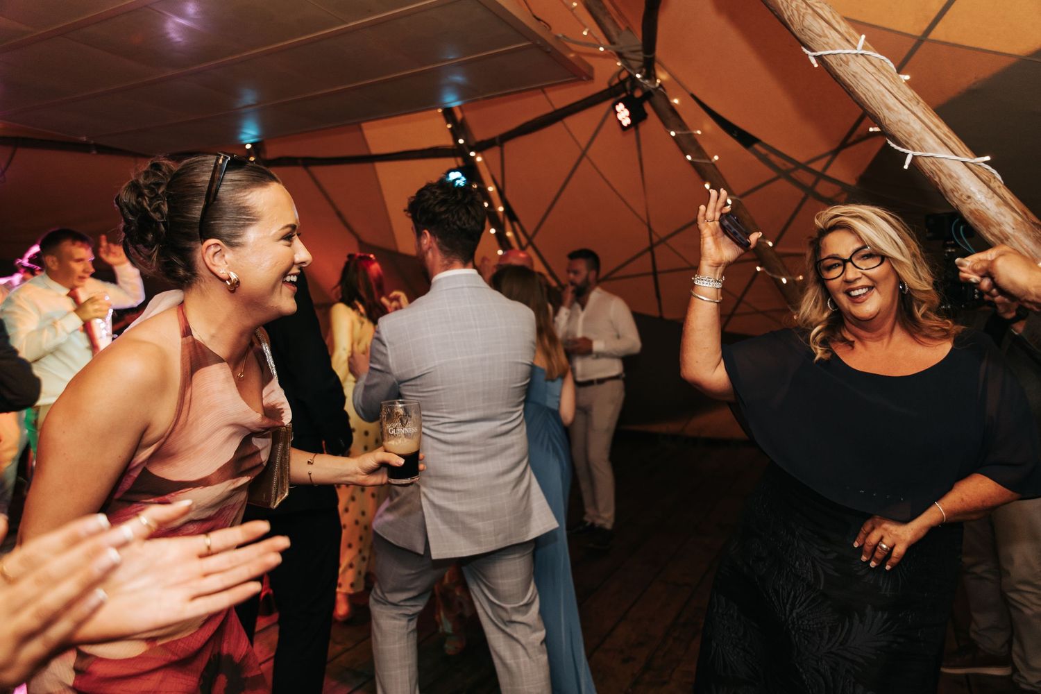Guests dancing and celebrating joyfully inside a tent at a lively wedding reception party.
