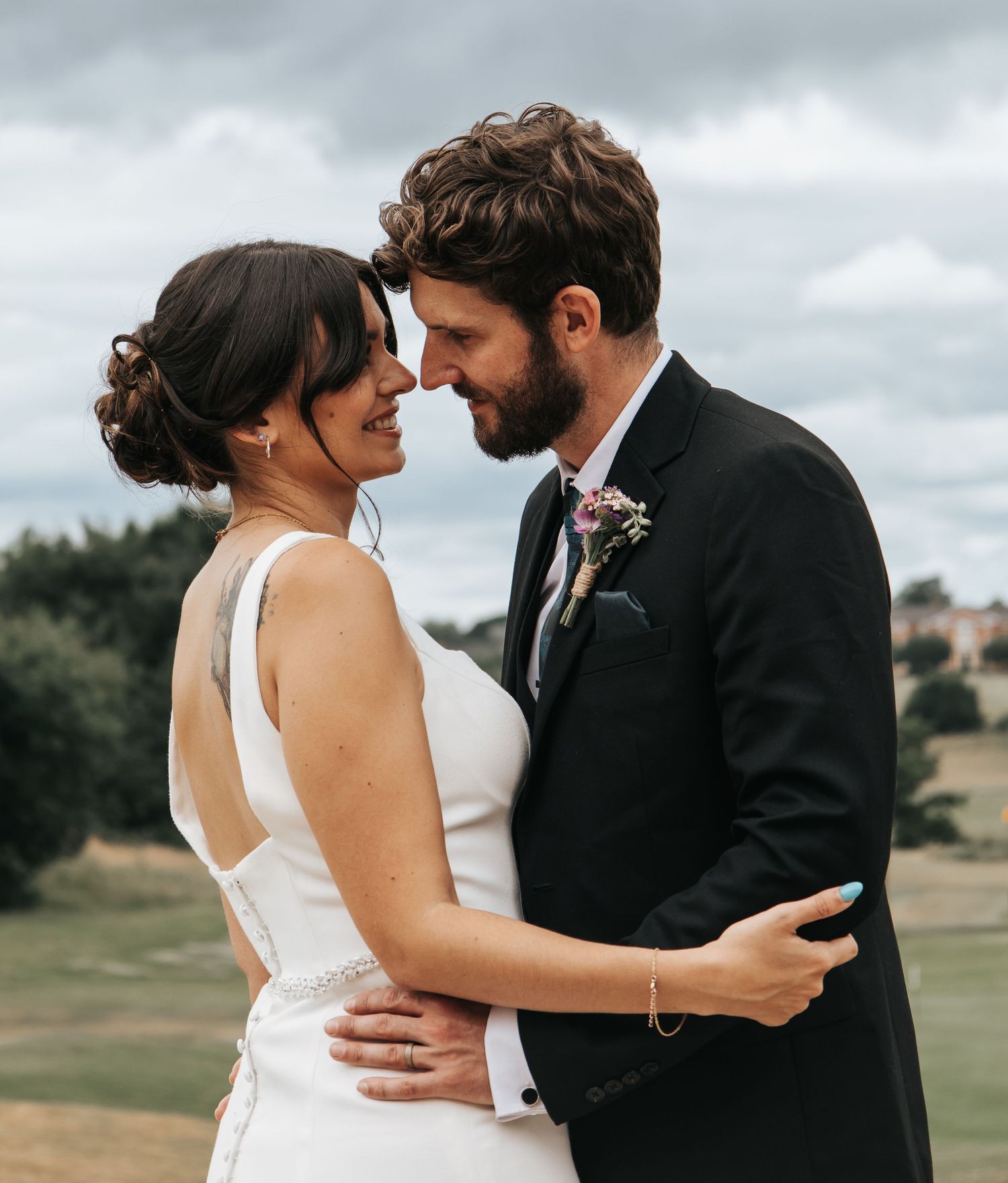 Wedding couple shares tender moments against a cloudy sky and natural landscape.
