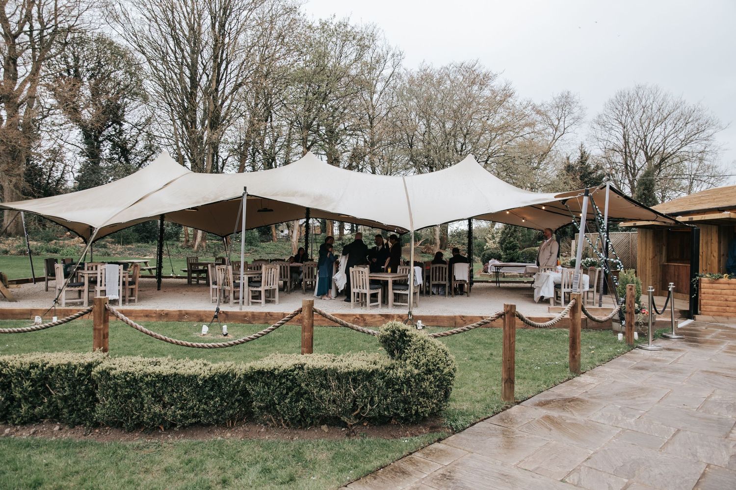 Elegant stretch tent marquee set up in a garden venue with rope fencing and wooden decking for outdoor events.