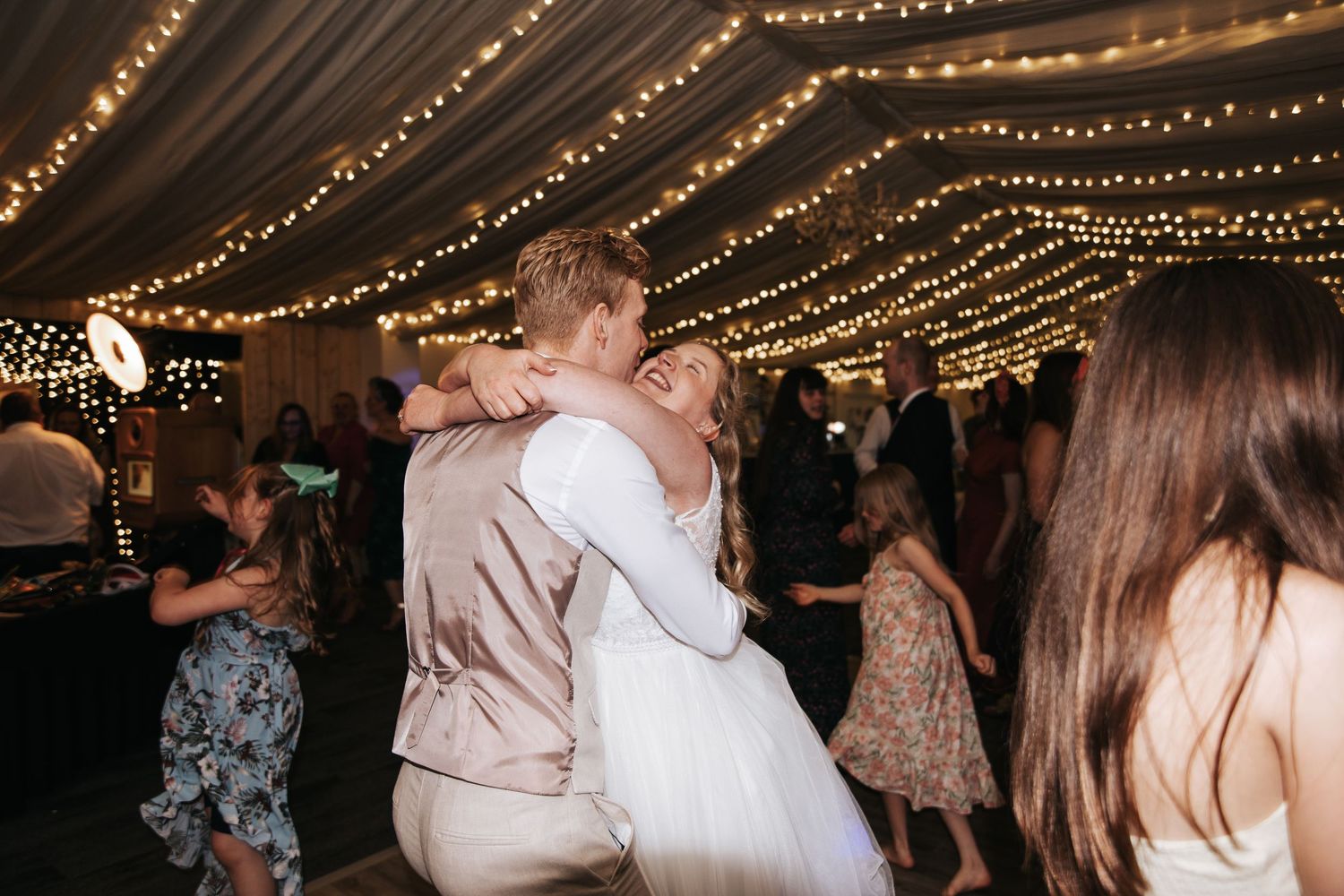 Bride and groom share a romantic first dance embrace under twinkling fairy lights at elegant wedding reception.