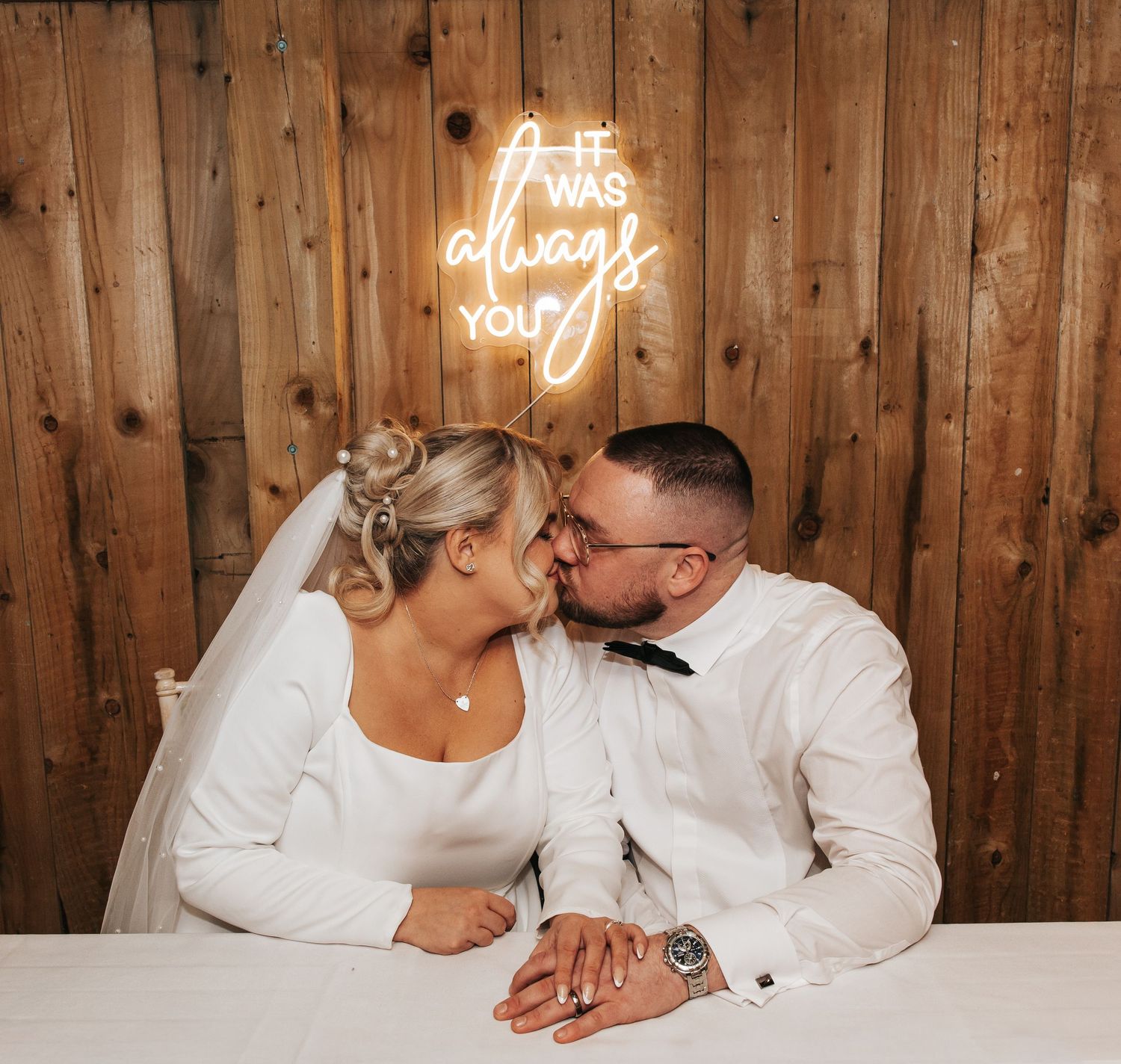 Romantic couple shares intimate moment under glowing neon 'always you' sign at wedding reception.