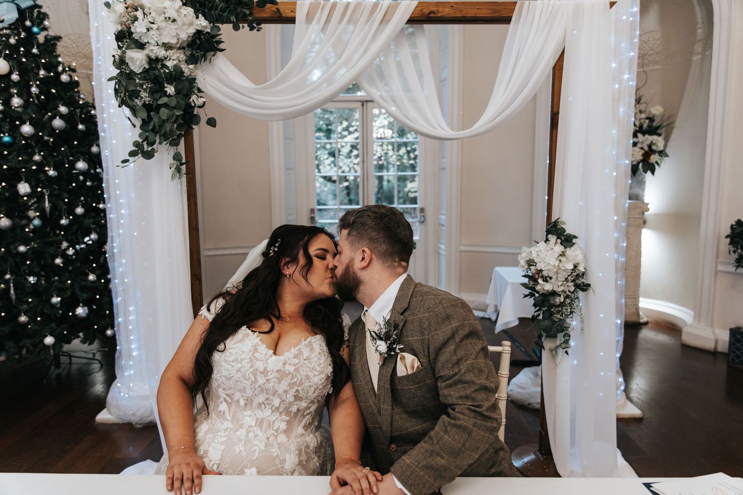 Romantic wedding scene with white drapes and twinkling lights in the background.