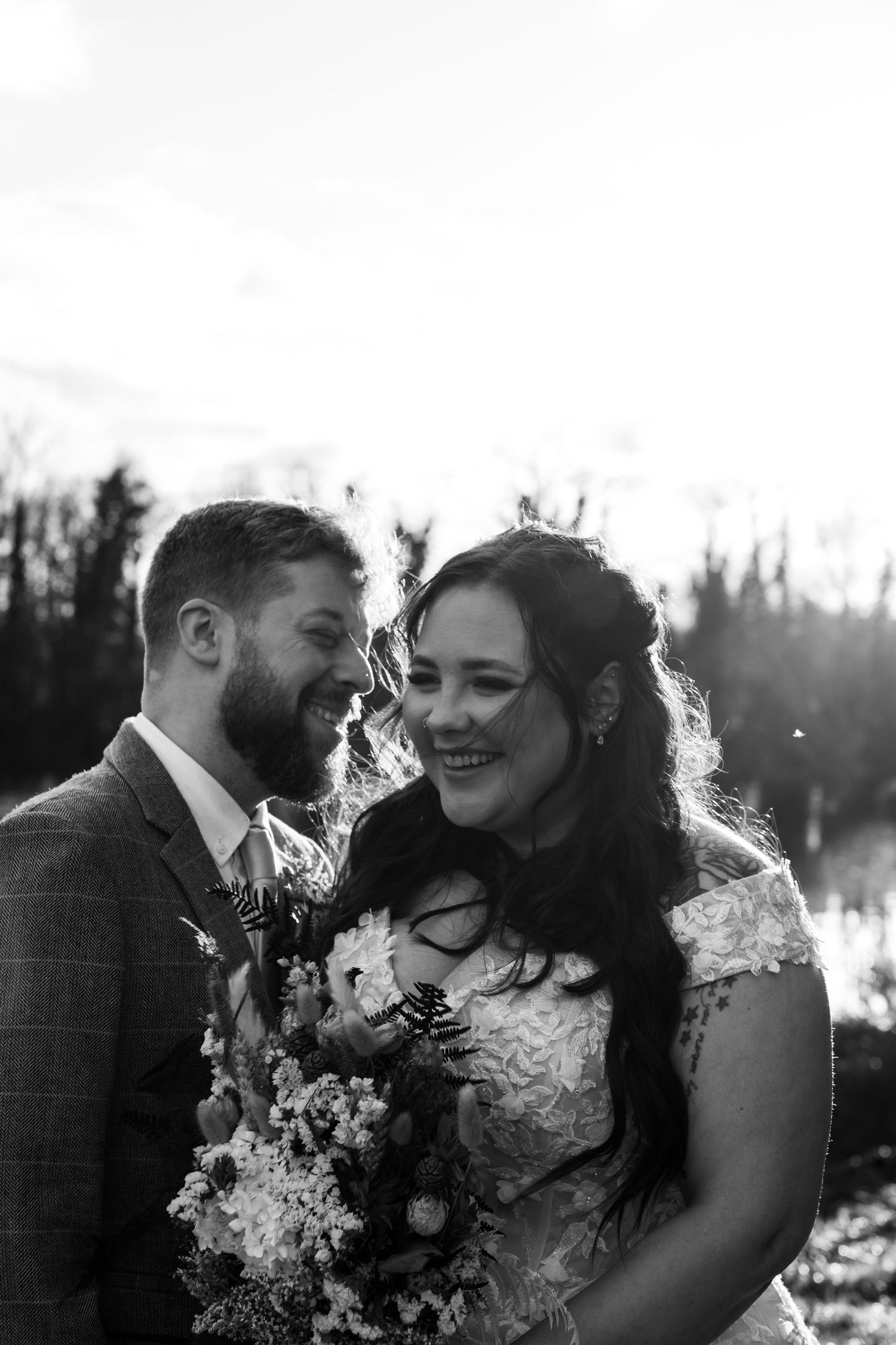 Intimate black and white portrait of wedding couple sharing joyful moment with bouquet.