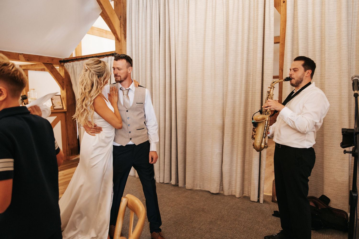 Bride and groom share a dance while a saxophonist performs at their elegant wedding reception.