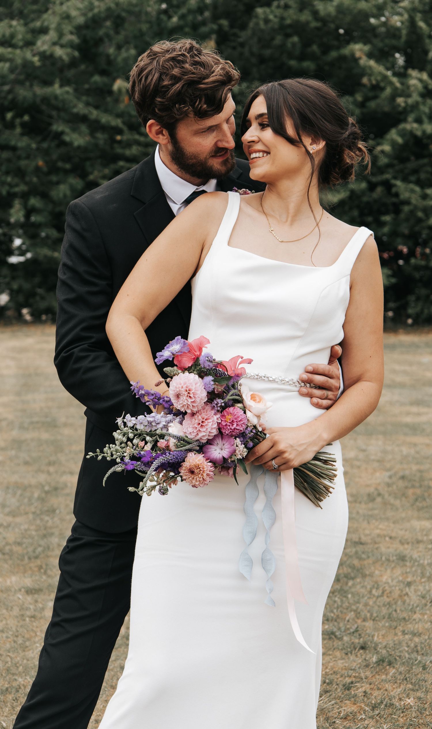 A tender wedding moment with a beautiful bouquet of pink and purple flowers.