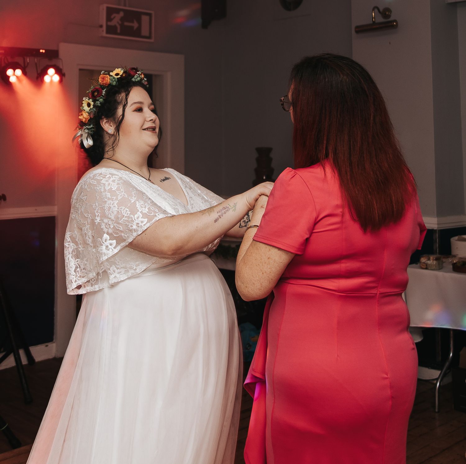 Two people in formal attire dance together at an indoor event with red mood lighting in the background.