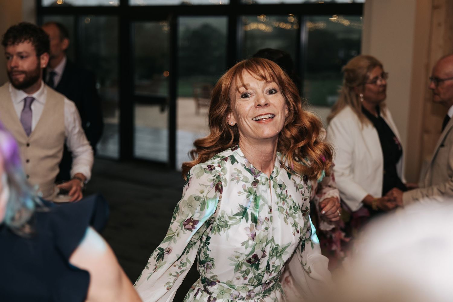 Woman in floral dress smiling and dancing at a wedding reception event.