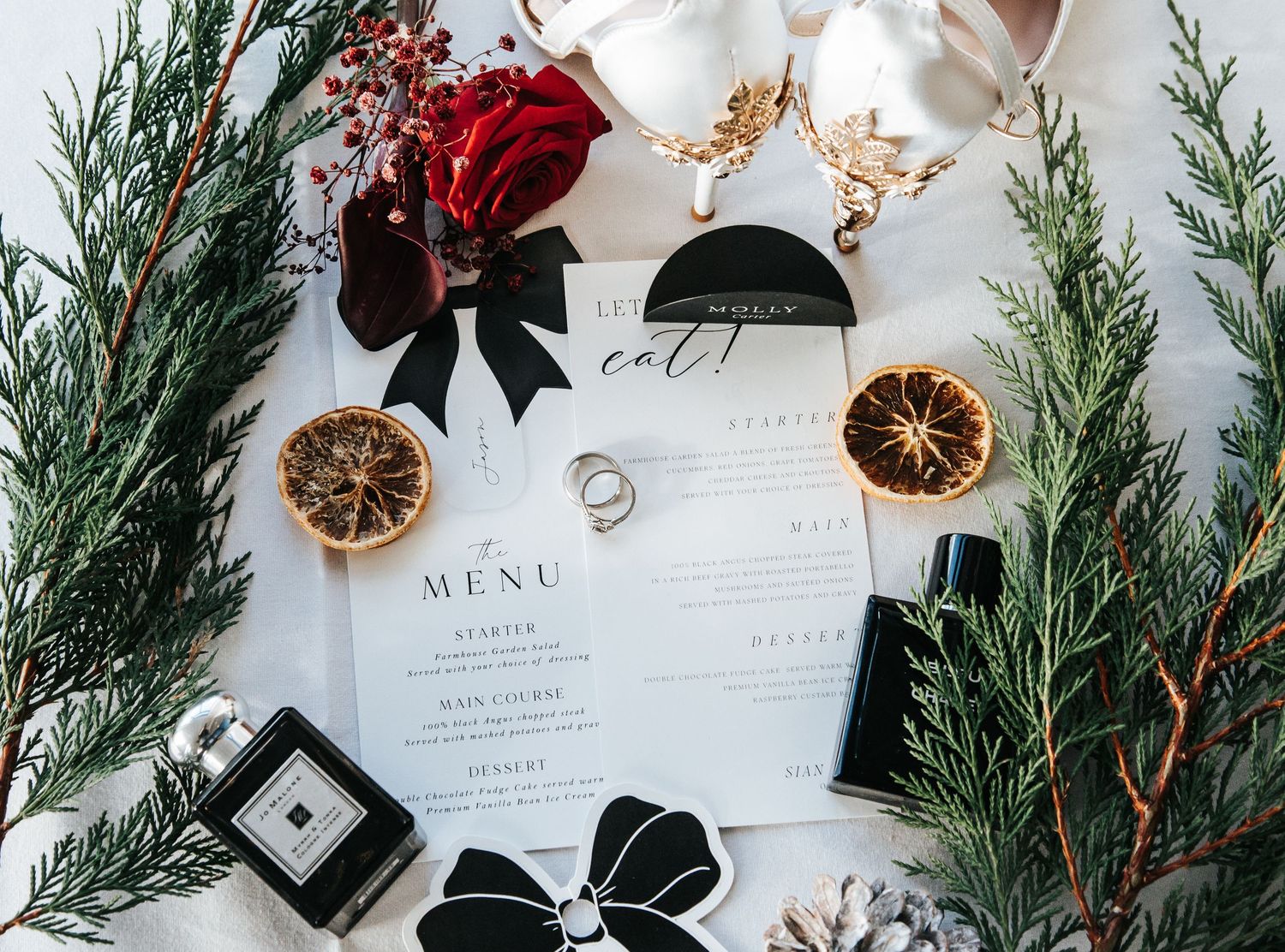Festive wedding stationery layout with evergreen branches and dried orange slices.