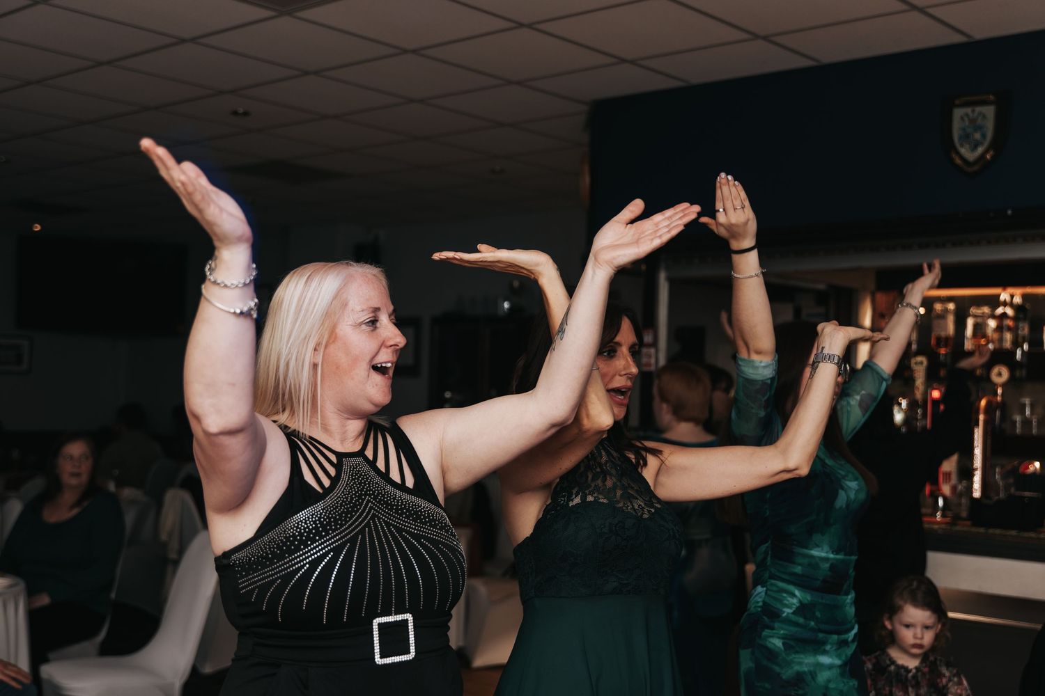 People dancing with raised hands at a nightclub party with dark lighting and energetic atmosphere.