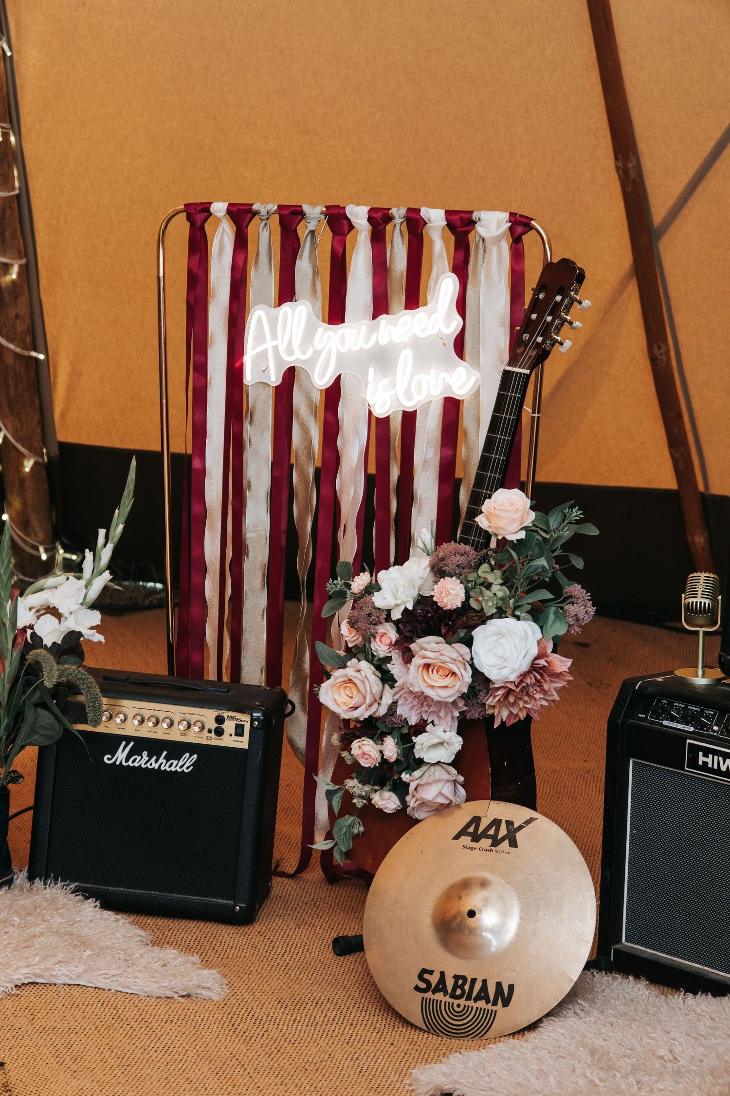 Music performance setup with Marshall amps, Sabian cymbal, and floral decor against striped background.