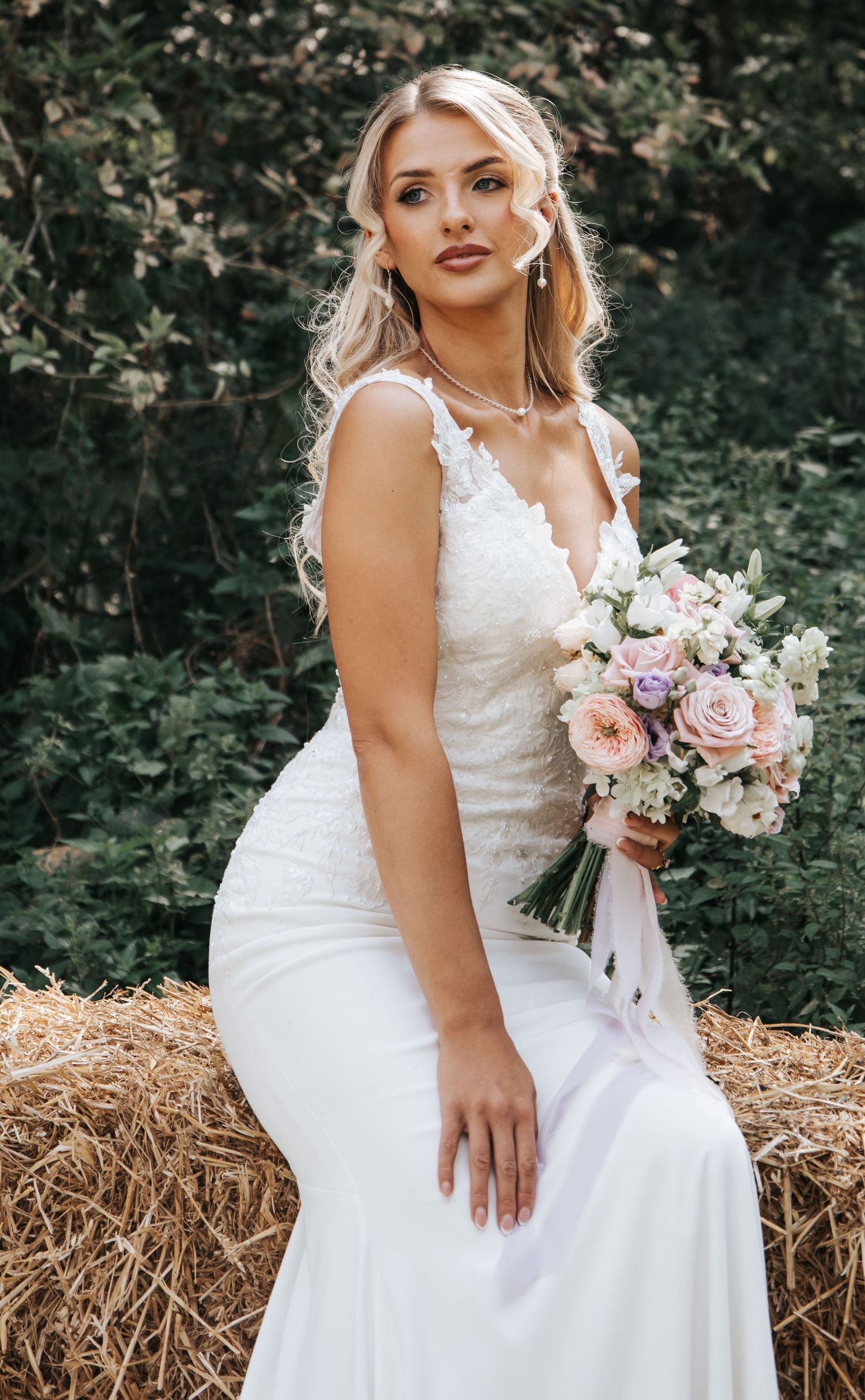 Romantic bridal portrait featuring soft pink and purple bouquet against natural woodland setting.