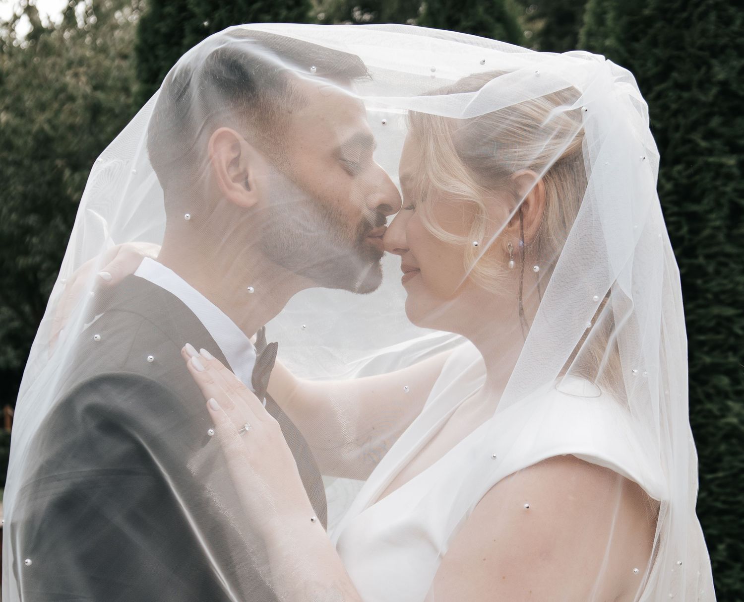 A romantic wedding moment captured under a flowing veil in soft natural light.