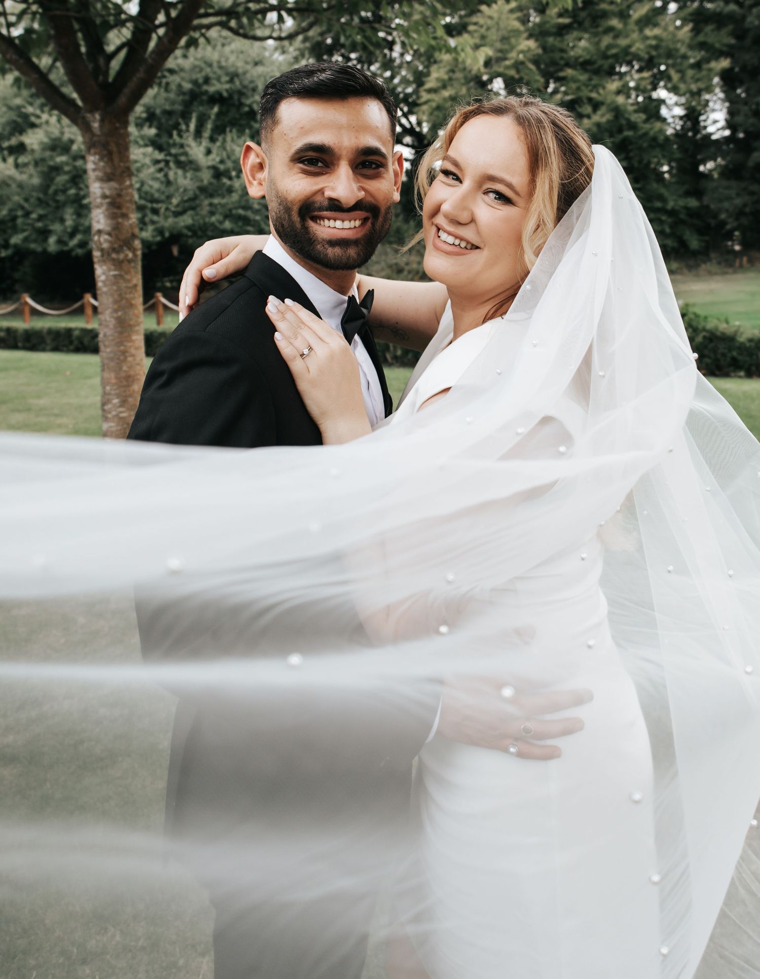 Romantic wedding portraits with flowing veil against a natural outdoor backdrop.