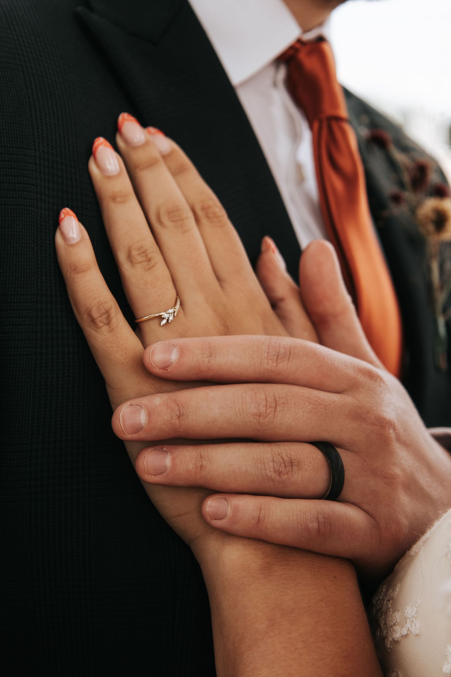 Wedding ring detail shots showing both traditional and black bands on intertwined hands.