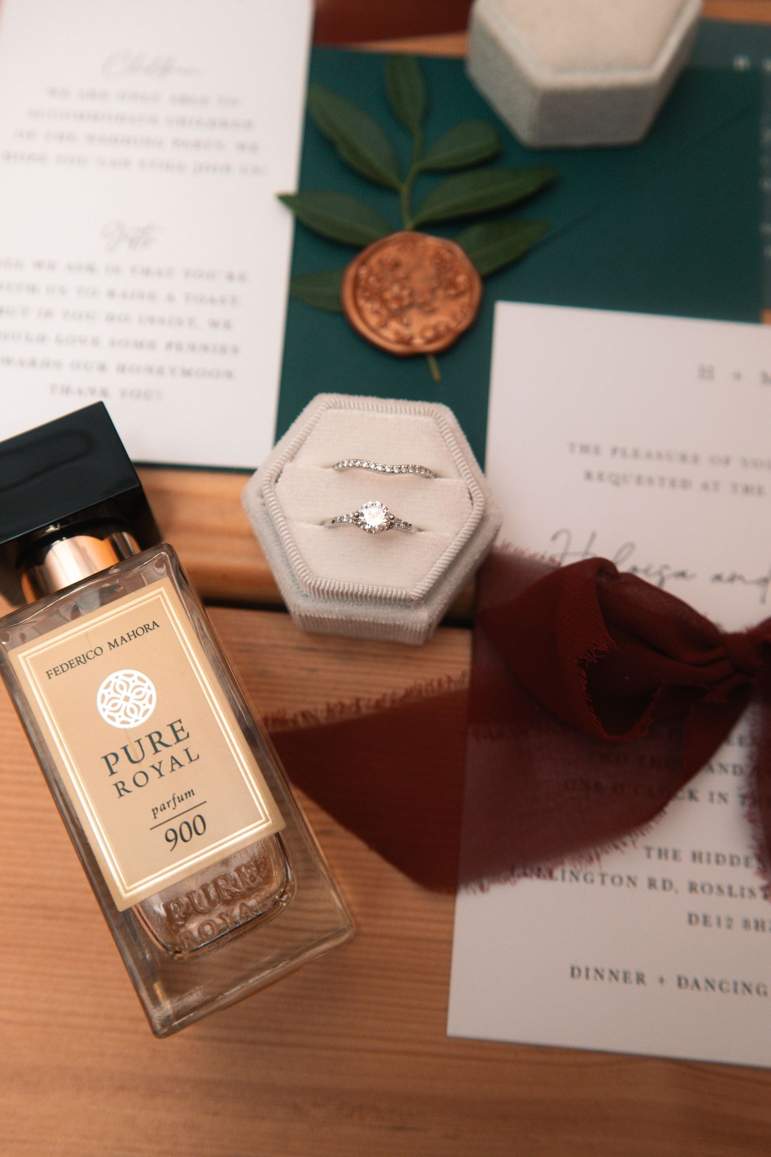 Wedding details including invitation suite, perfume bottles and ring box arranged on wooden surface.