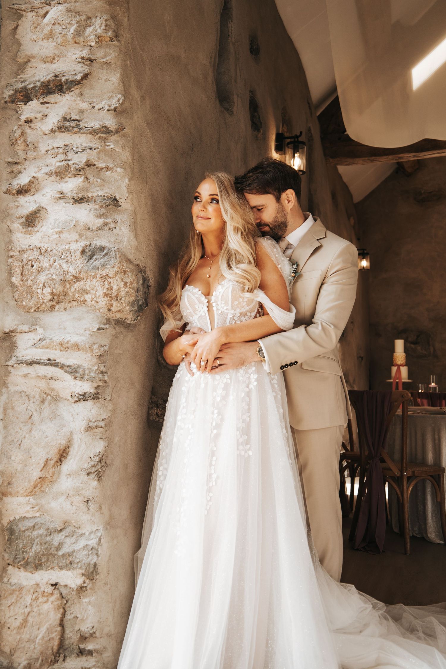 Wedding couple poses for romantic photos in front of rustic stone wall with natural lighting.