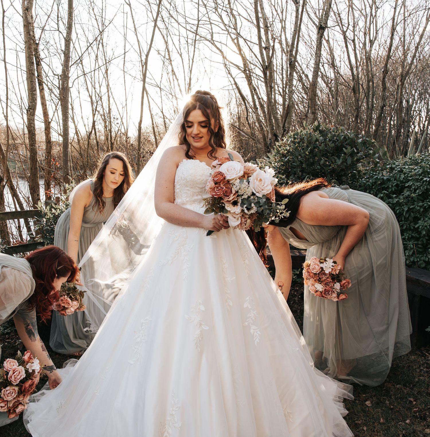 A wedding party poses outdoors in winter with bridesmaids in neutral dresses and a flowing white bridal gown.