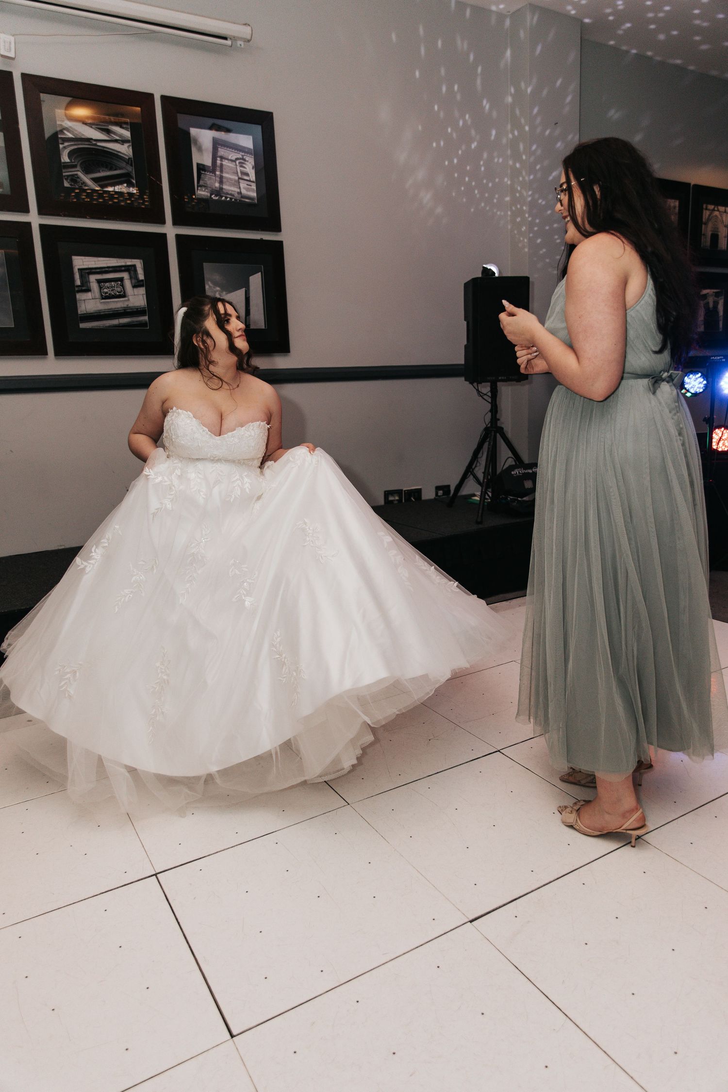 A bride in a flowing white gown twirls on a white dance floor while being photographed.