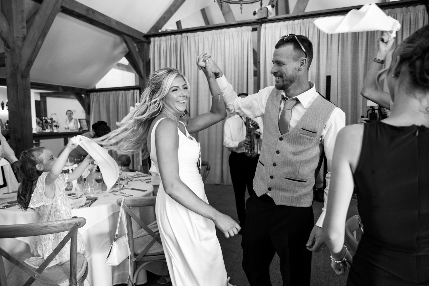 Black and white photo of a bride and groom dancing joyfully at their wedding reception in a rustic venue.