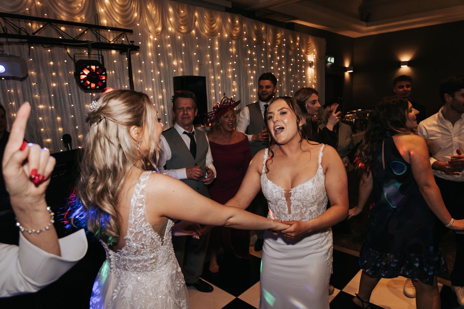 Wedding guests dance and celebrate on the dance floor under twinkling string lights at an evening reception.