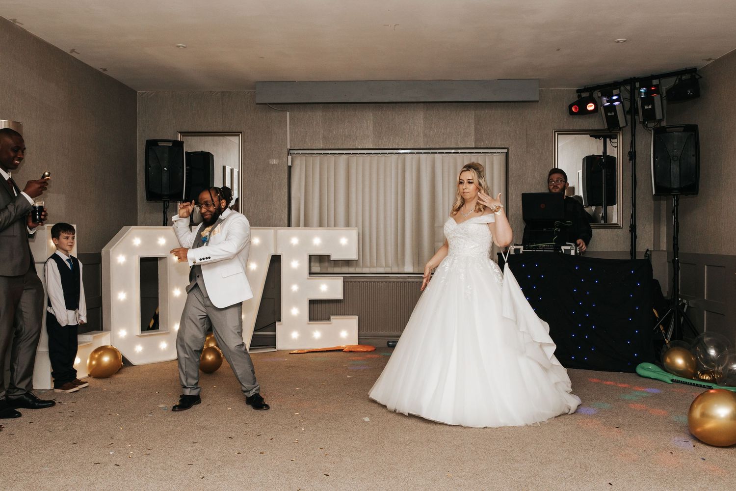 A wedding couple performs their first dance in a reception hall surrounded by guests and photographers.