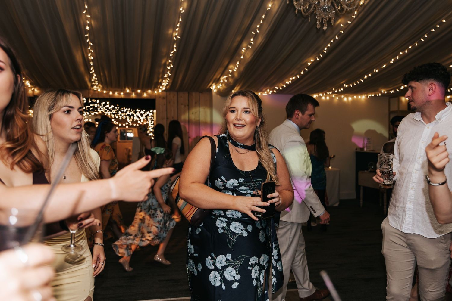 Guests dancing and socializing at an elegant indoor wedding reception with fairy lights.