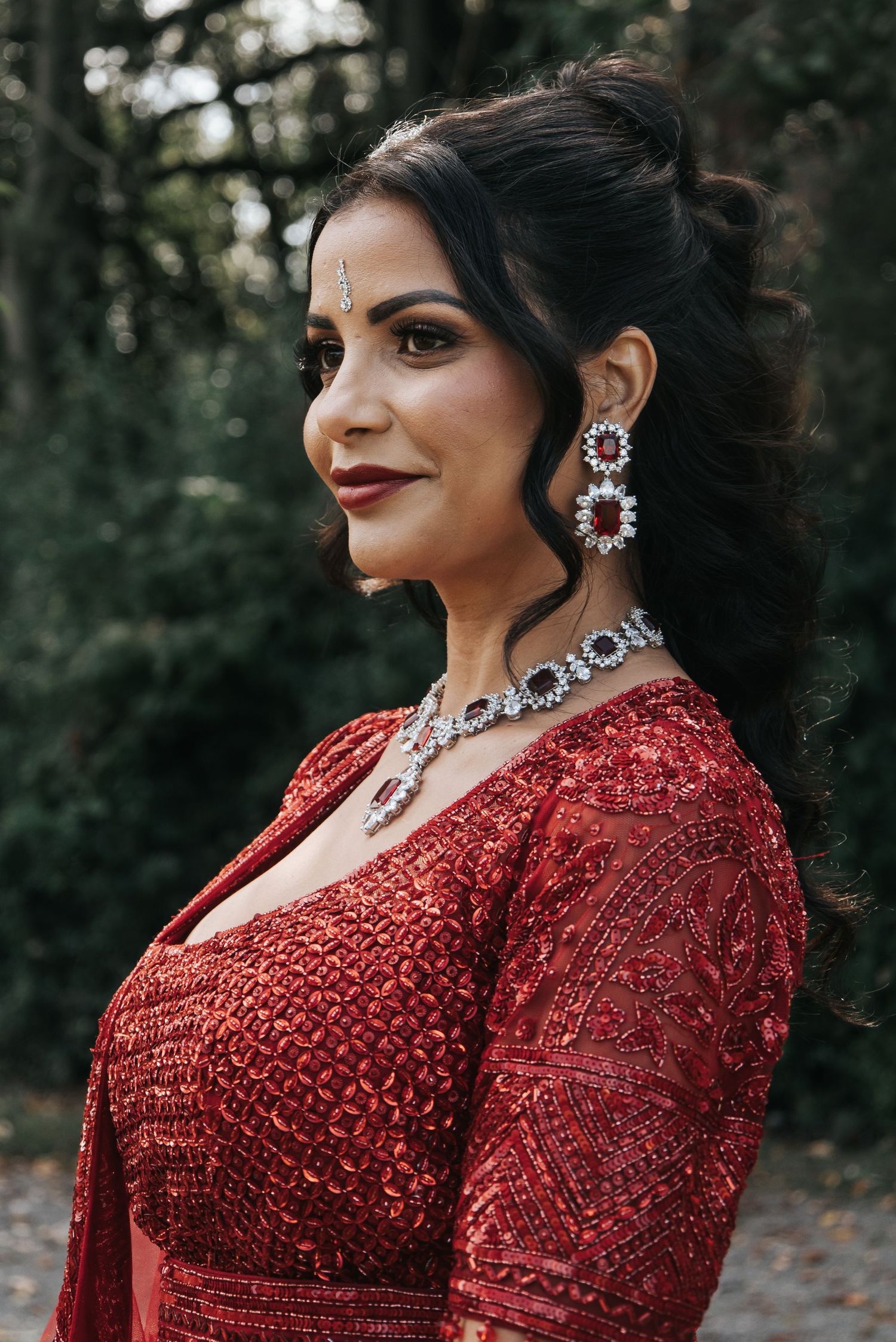 Glamorous portrait series in a sparkly red gown with statement jewelry against a forest backdrop.
