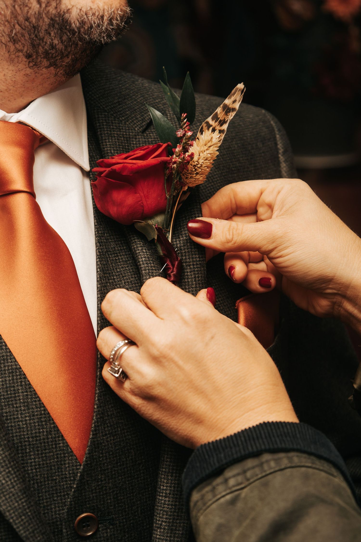 Close-up of hands pinning a red boutonniere on a dark suit lapel.