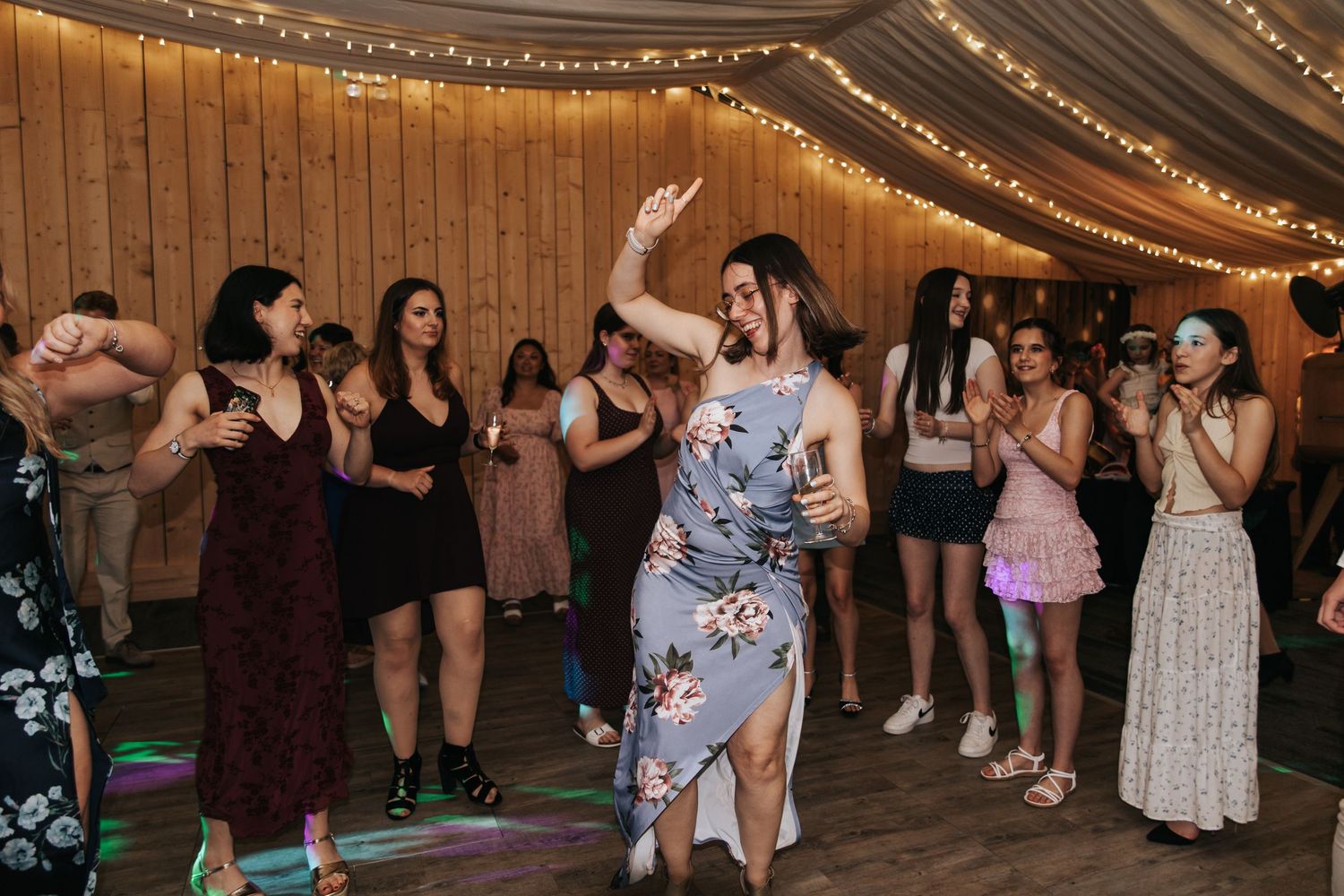 Guests dancing and celebrating at a rustic wedding reception with string lights.