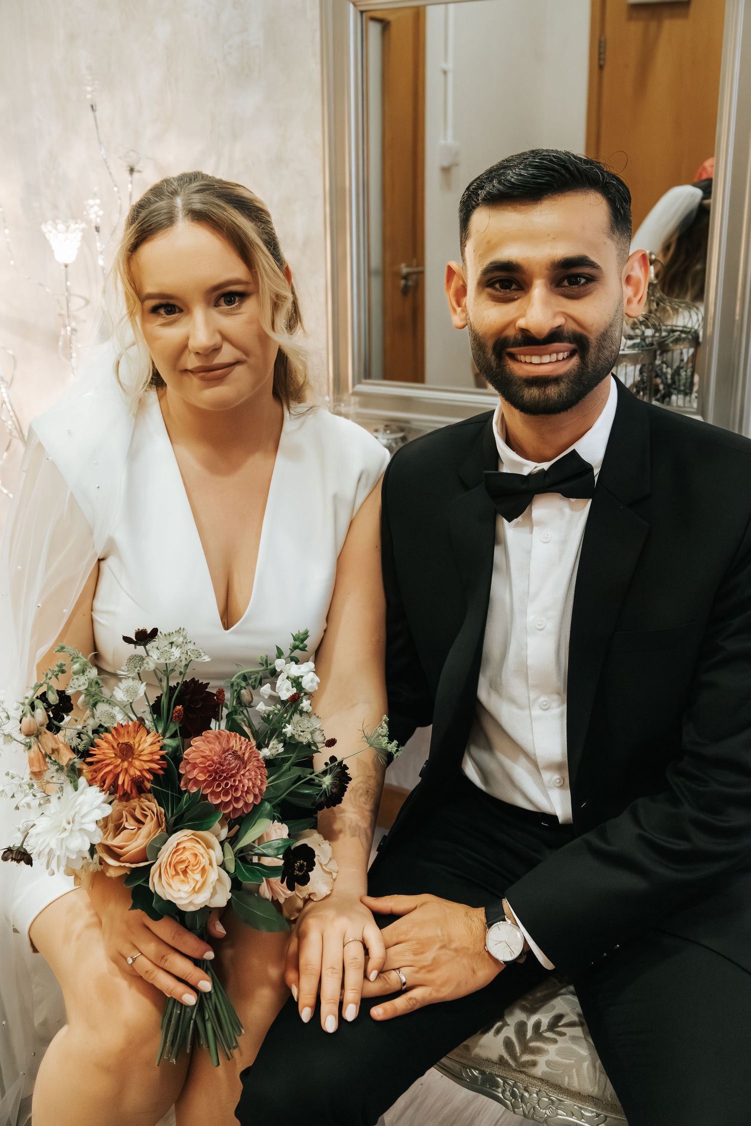 Couple posing with floral bouquet in formal wedding attire.
