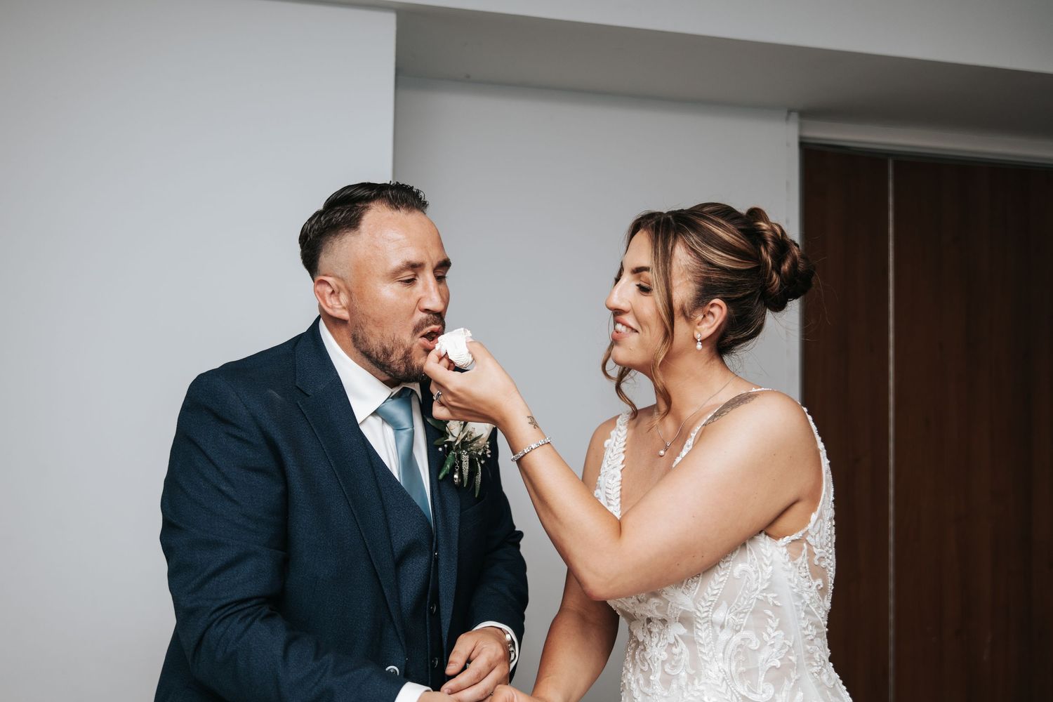 Bride adjusting groom's boutonniere on wedding day, both smiling in elegant attire.