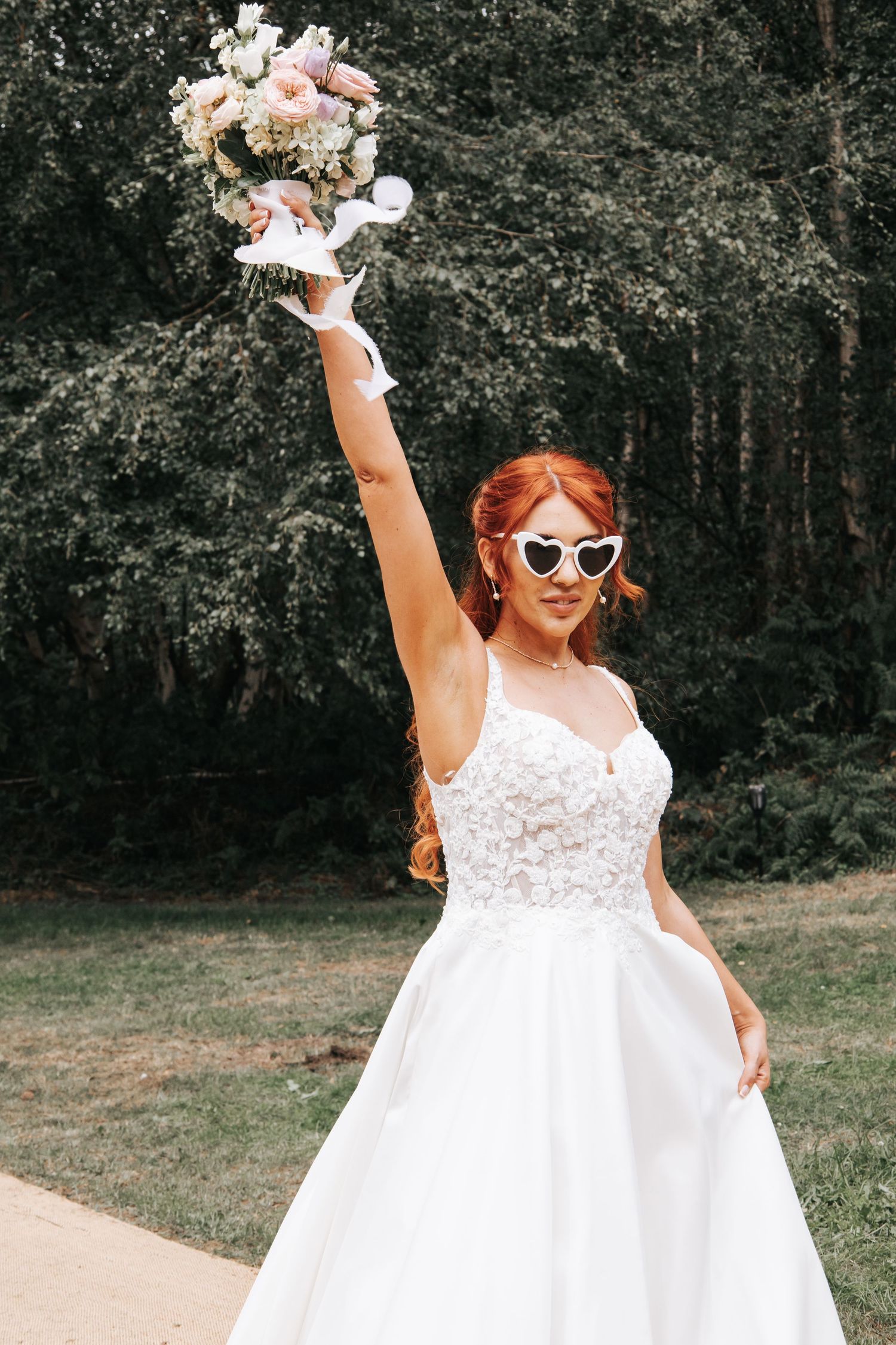 Triumphant wedding day pose with raised bouquet against forest backdrop.