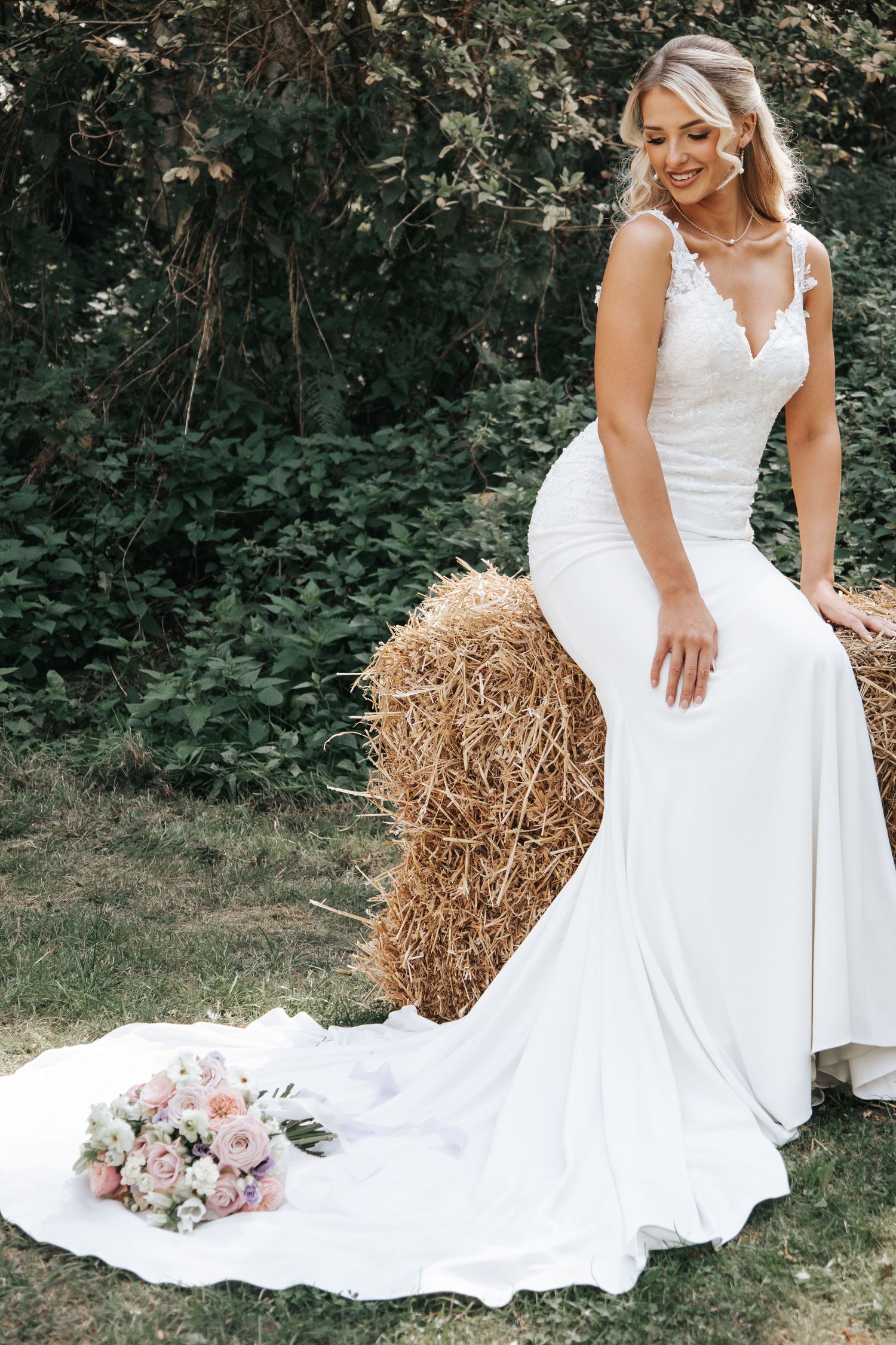 Elegant outdoor bridal portrait with flowing train and rustic hay bale setting.