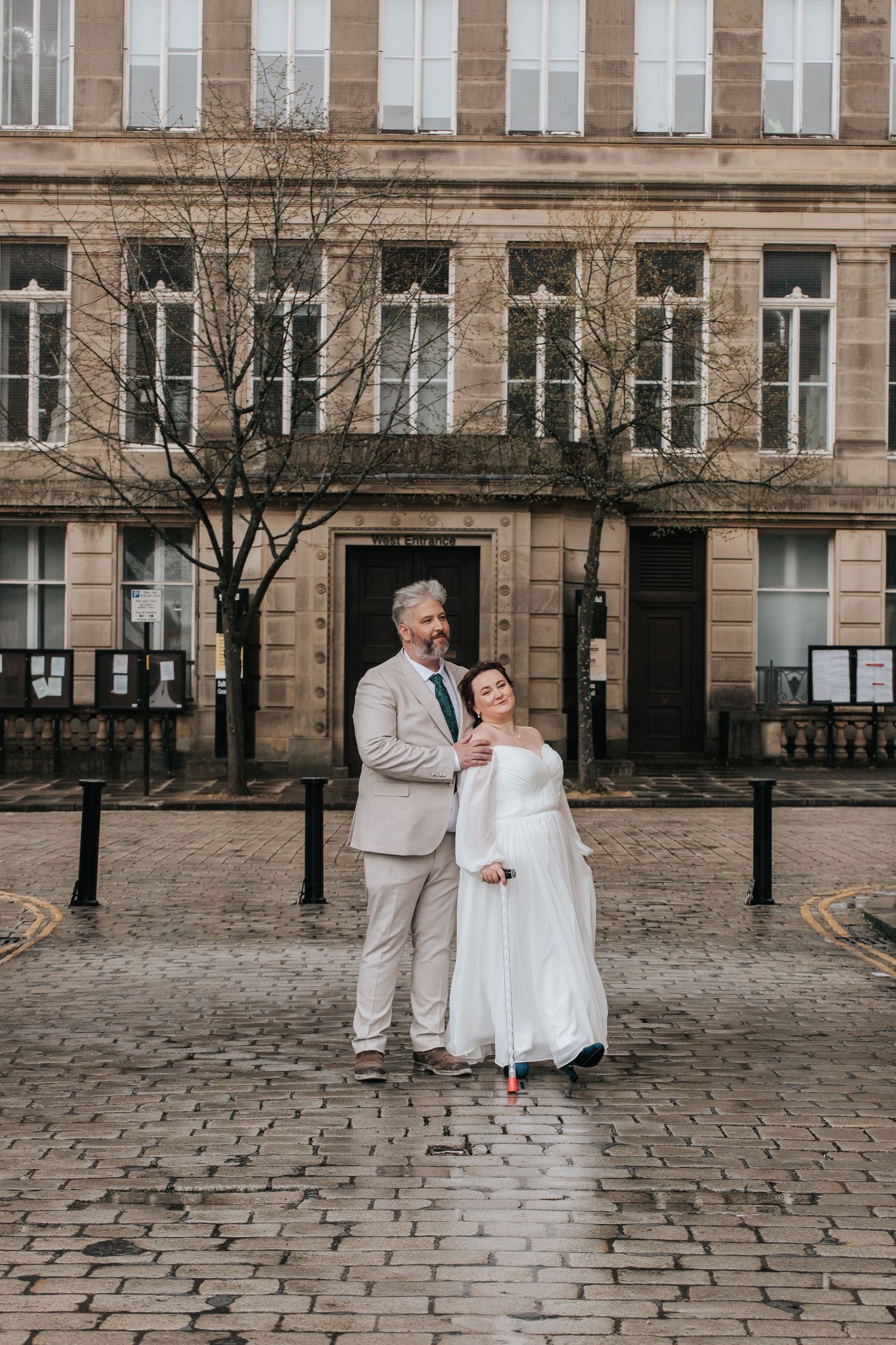 Bride and groom pose on cobblestone street outside historic stone building on their wedding day.