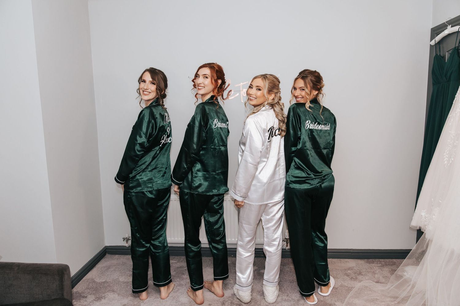 Bridal party wearing matching silk robes in emerald green and white pose in getting ready room.