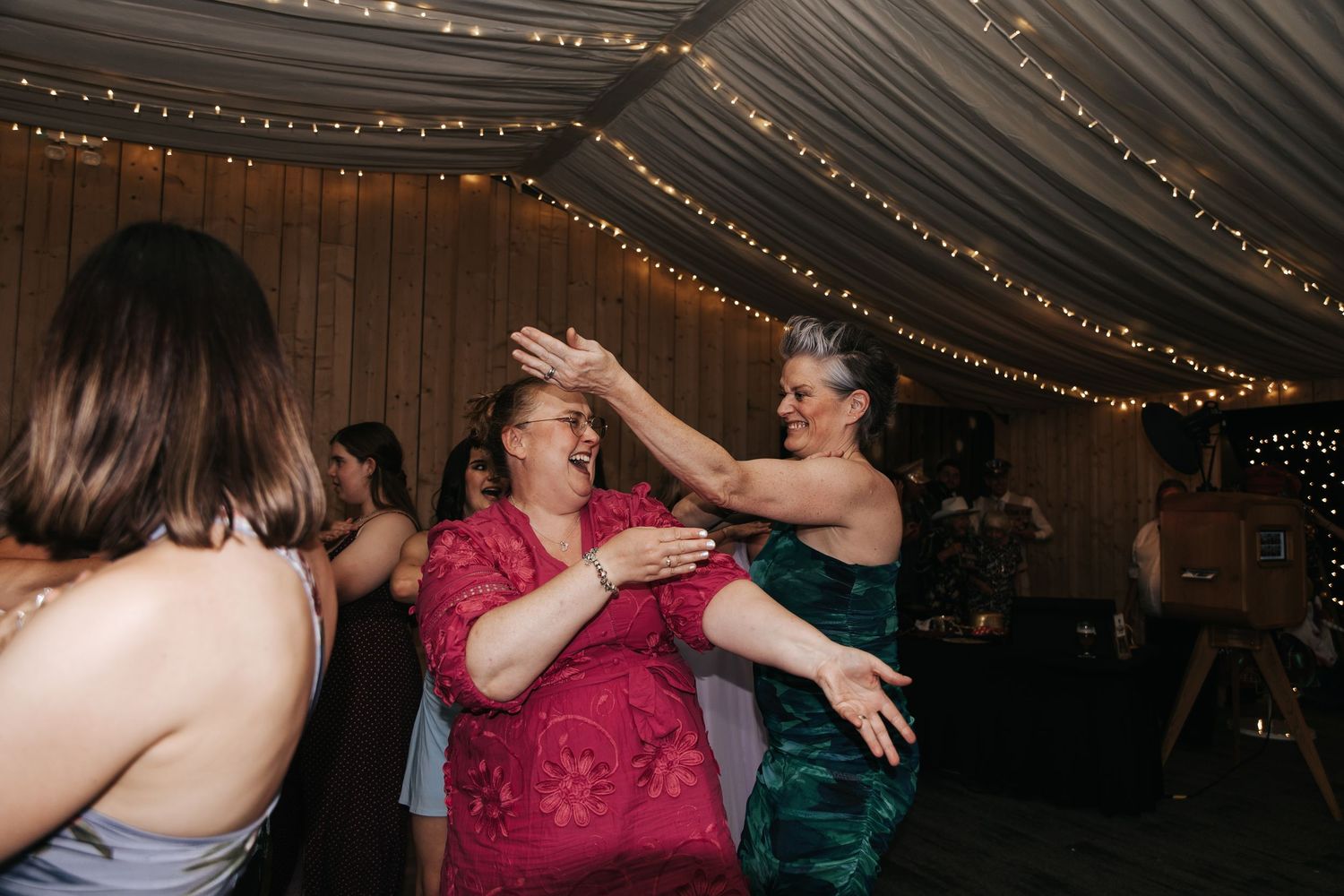 Two women dancing together at a wedding reception under fairy lights in a marquee.