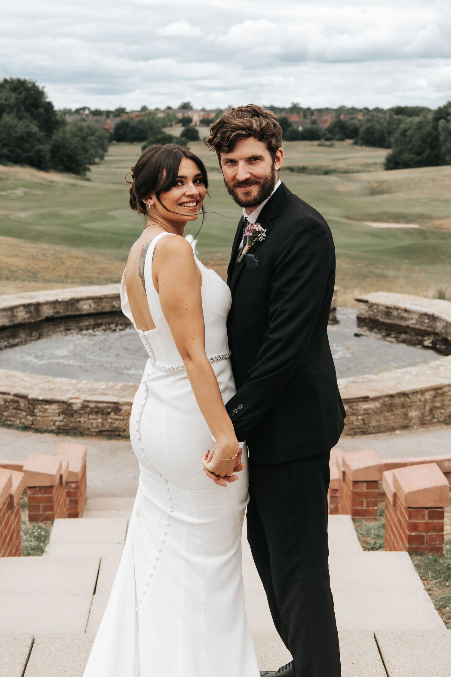Romantic wedding couple embraces on stone patio with scenic landscape view.
