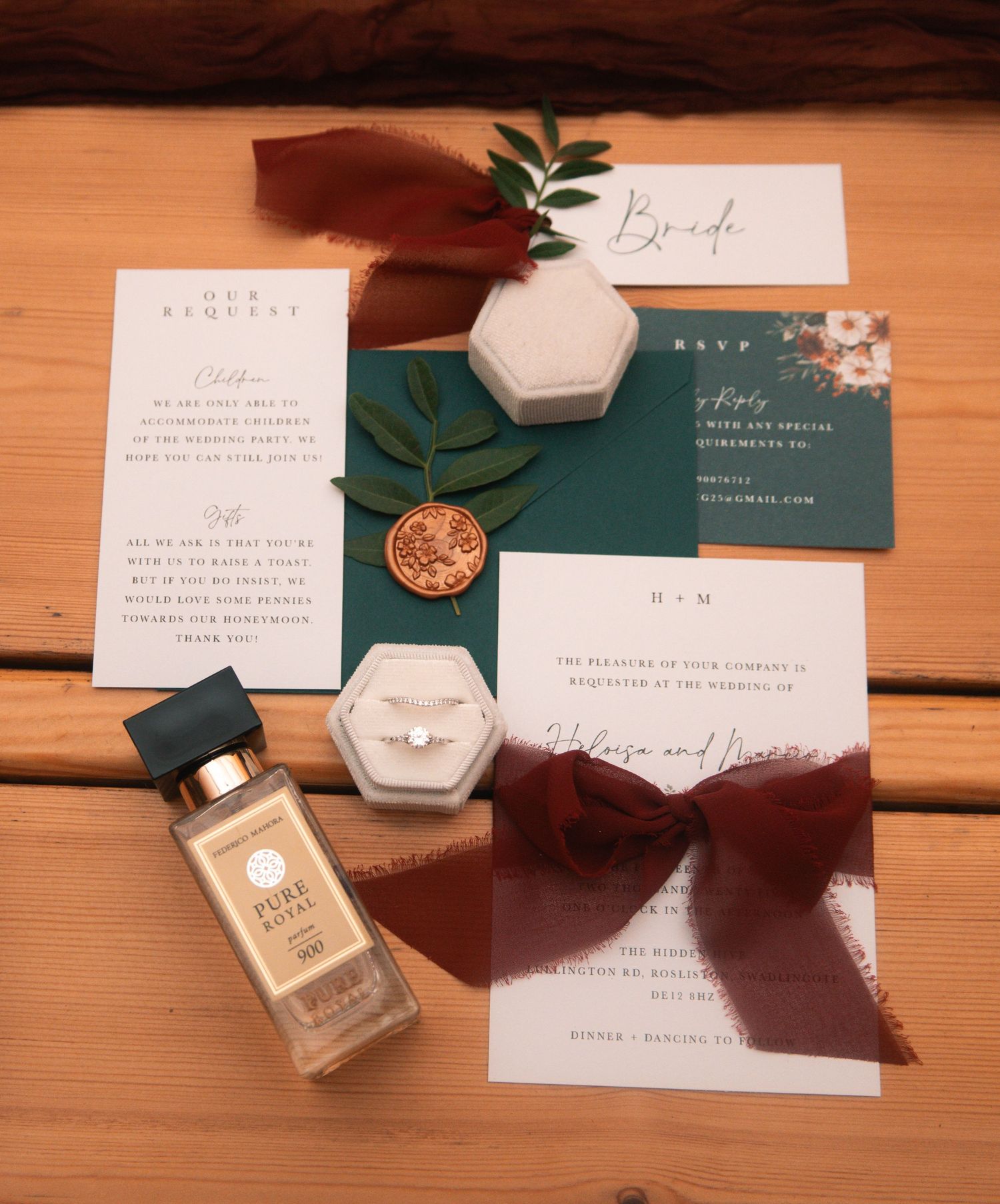 Wedding invitation suite with emerald green accents and perfume bottles on wooden table.