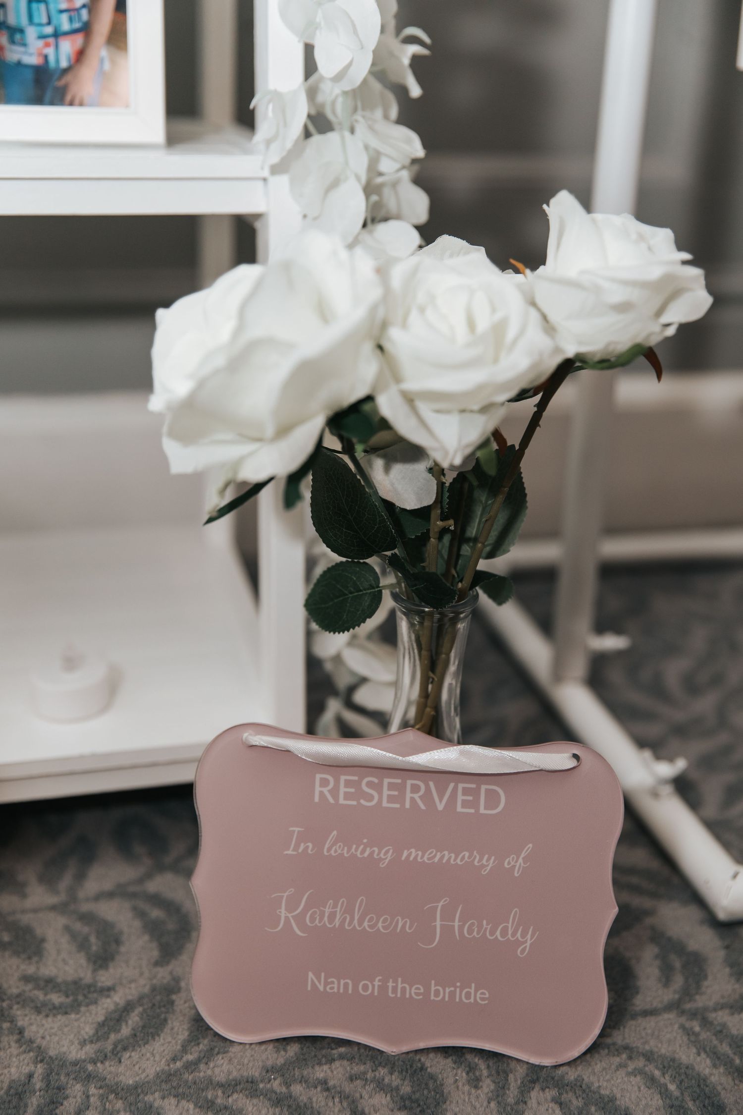 Reserved memorial sign for Kathleen Hardy, nan of the bride, displayed with white roses at a wedding reception.