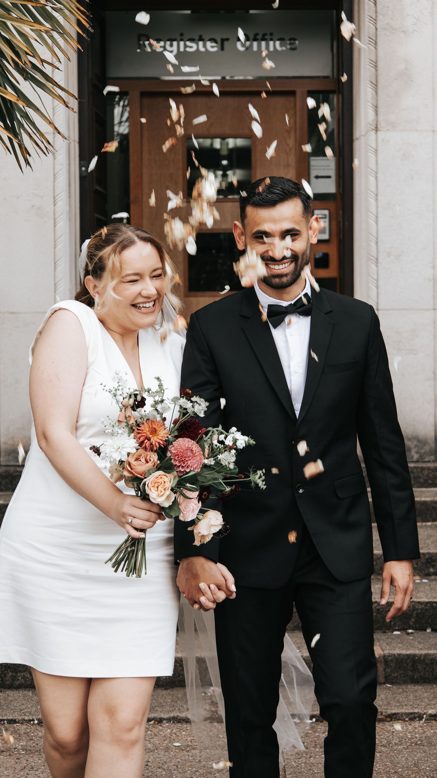 Wedding couple celebrating with confetti outside a registry office entrance.