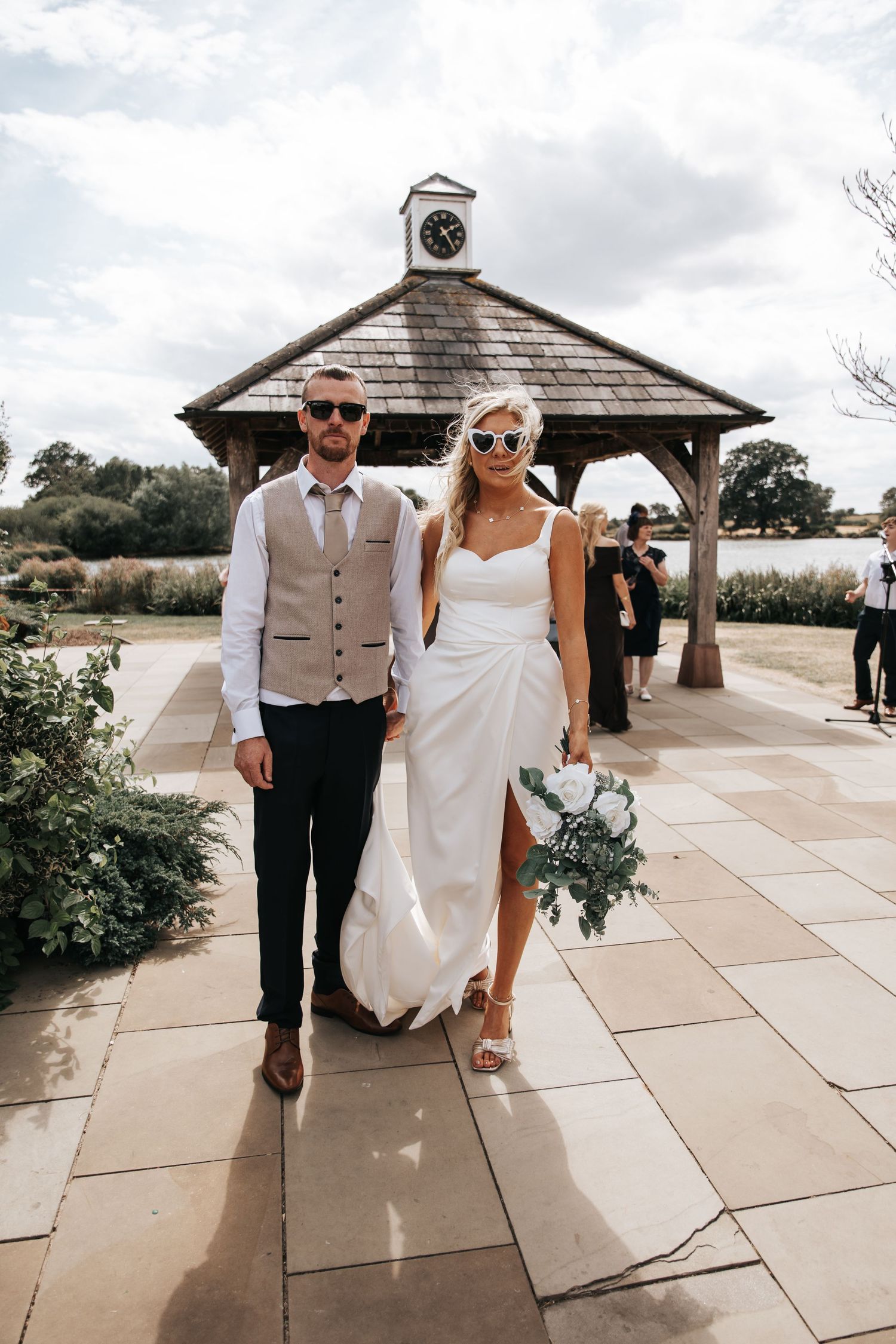 Bride and groom walking hand in hand outside a rustic gazebo with clock tower on their wedding day.