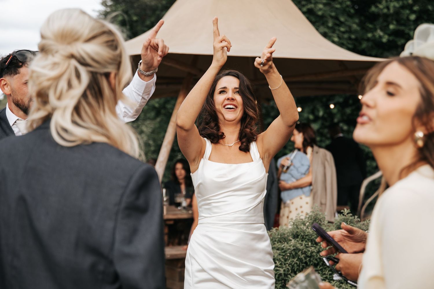 Bride in white dress dancing joyfully with raised arms at outdoor wedding reception celebration.