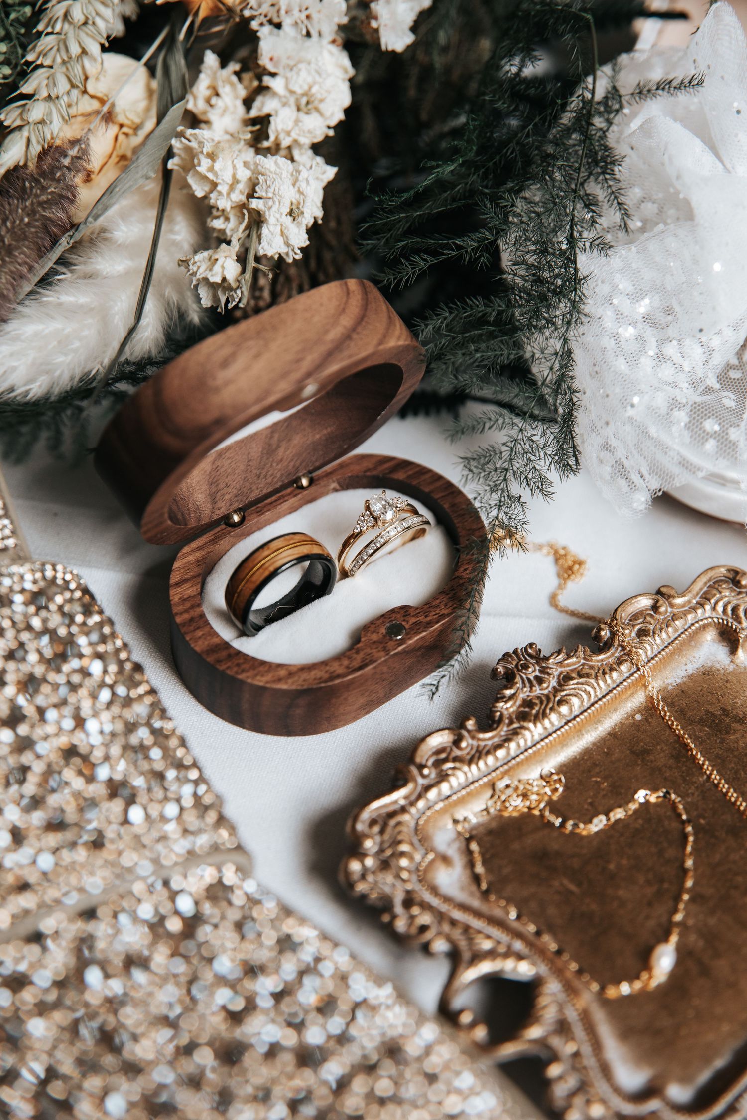 Wedding accessories including rings, jewelry and wooden decor arranged with floral elements.