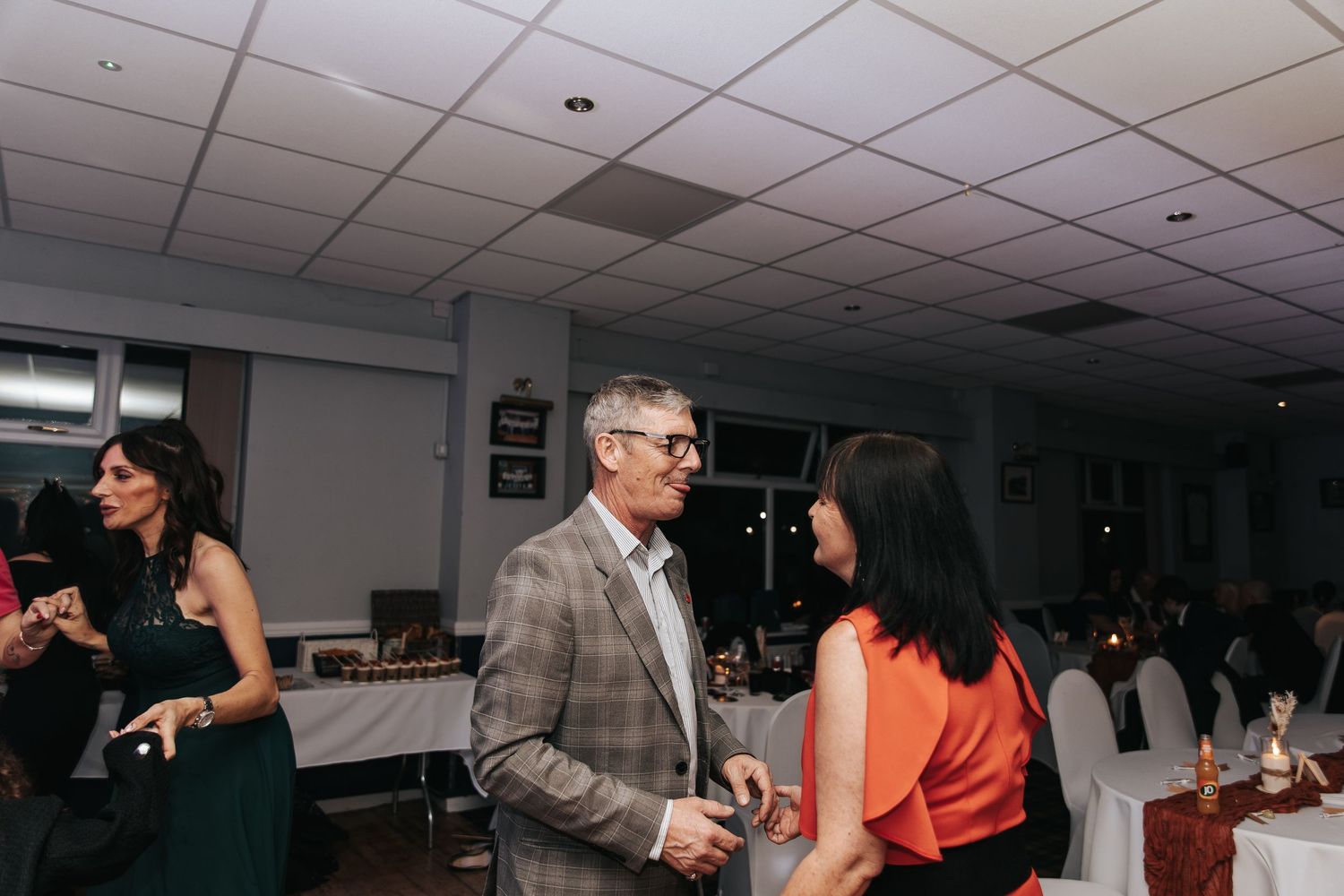 People dancing and socializing at an indoor event with fluorescent lighting and drop ceiling tiles.