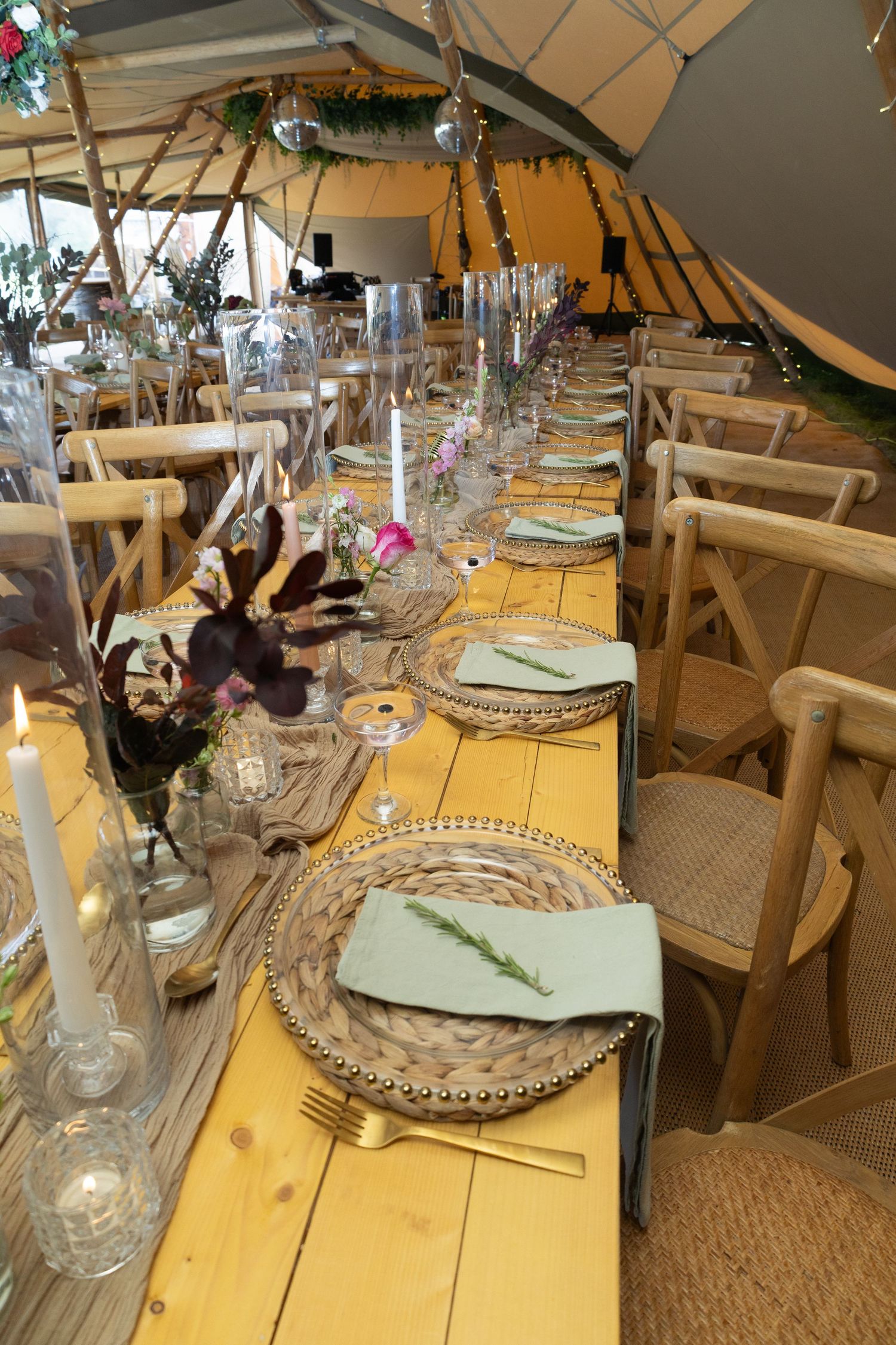 Long dining table setup inside a tent with wooden chairs and elegant place settings.