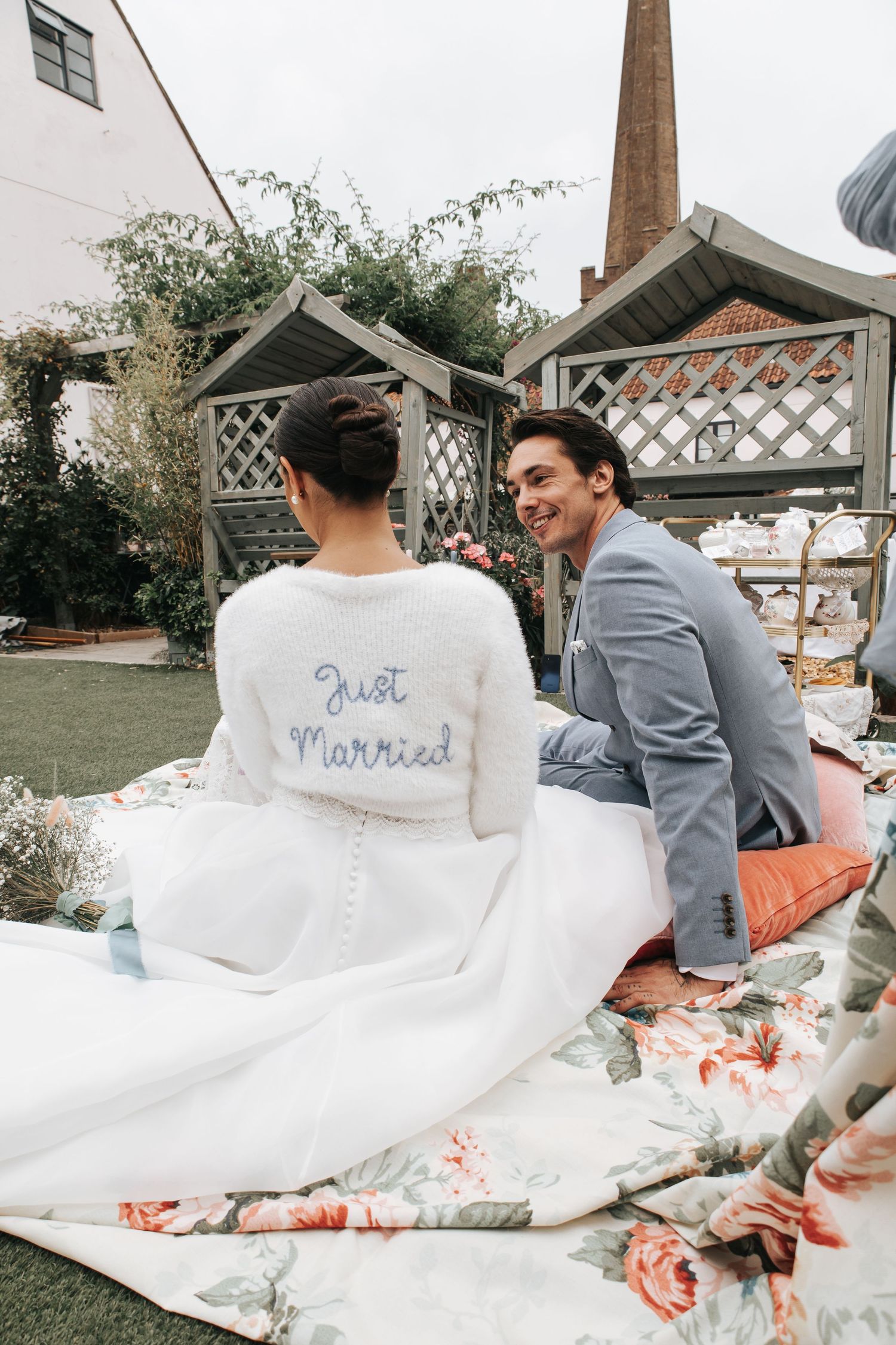 Couple relaxing on picnic blanket with bride wearing 'Just Married' shawl.