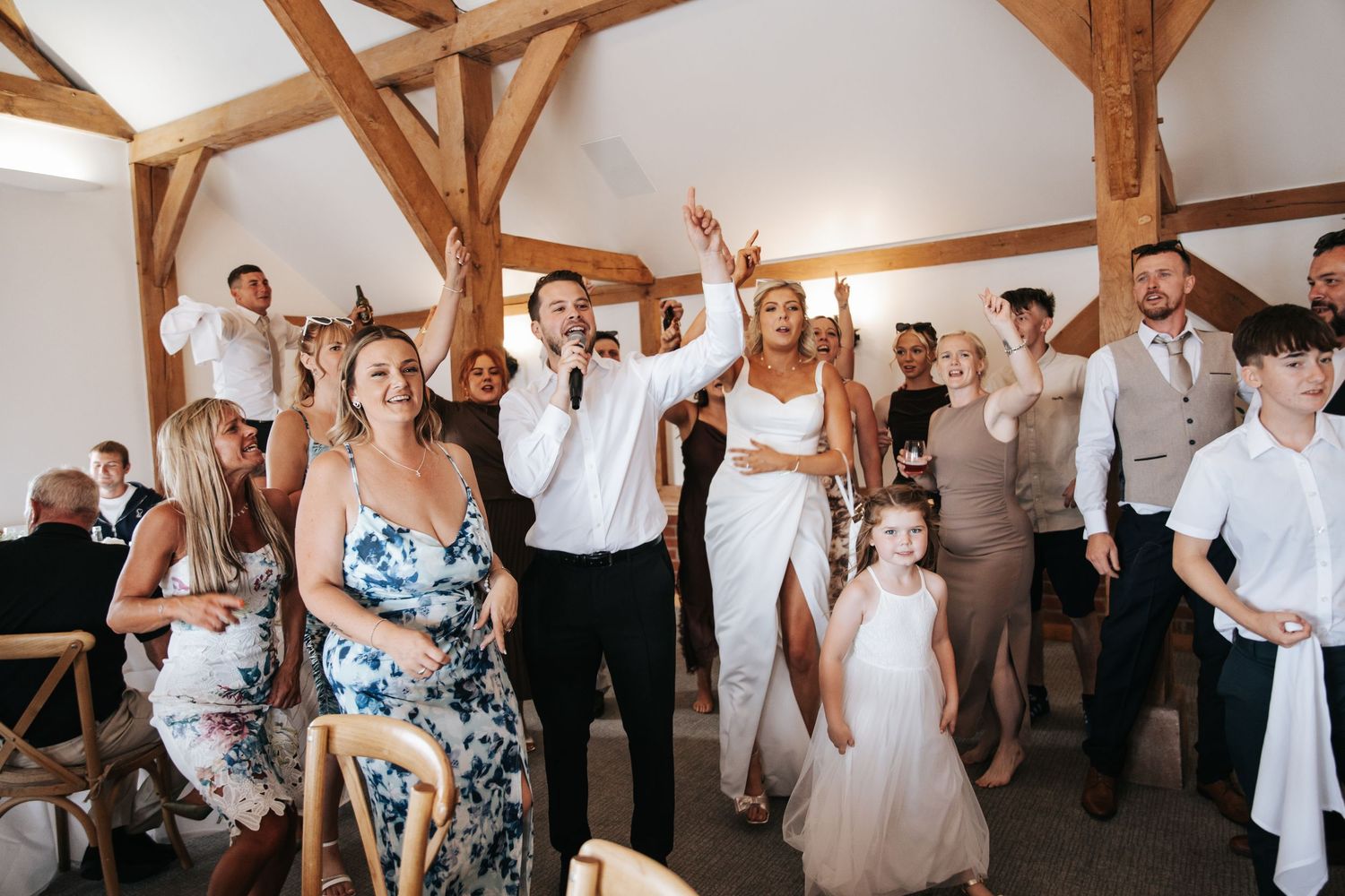 Joyful wedding reception scene with bride and groom celebrating among guests in a rustic barn venue.
