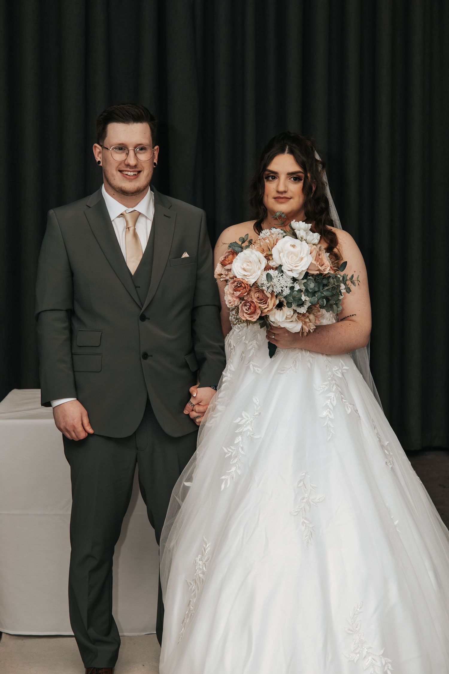 Formal wedding portrait featuring couple with pink floral bouquet against dark backdrop.