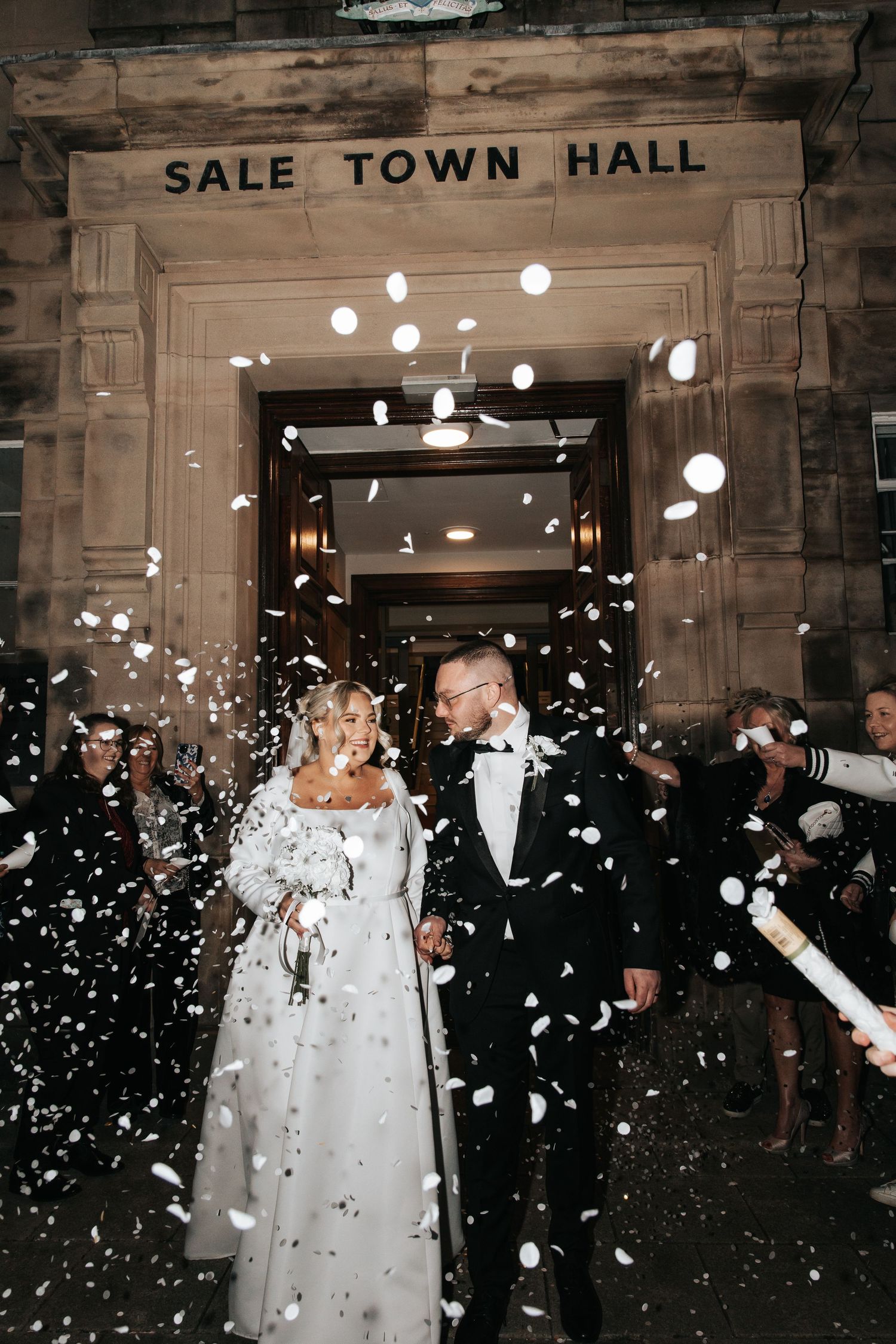 Newlyweds exit Sale Town Hall amid a joyful shower of white confetti on their wedding day.